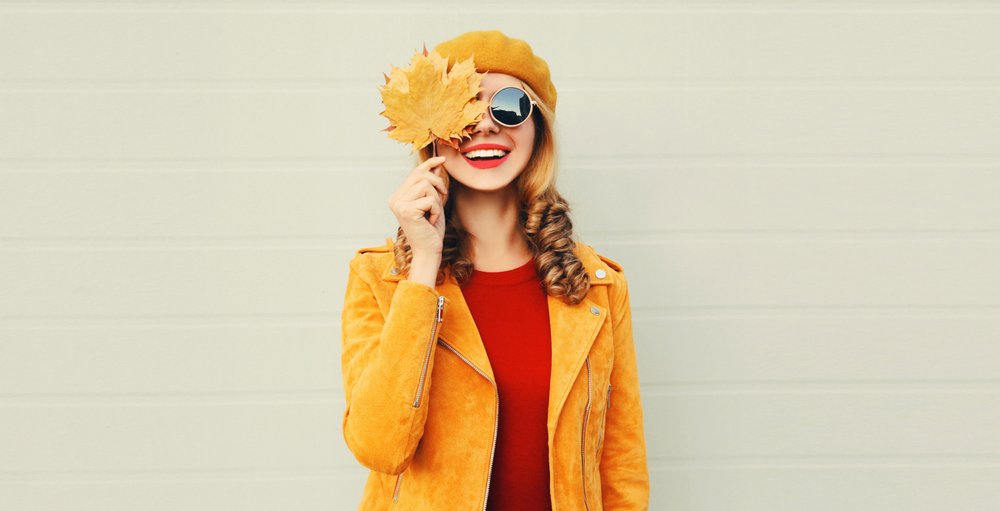 A happy smiling woman holding in her hands yellow maple leaves. | Photo: Shutterstock