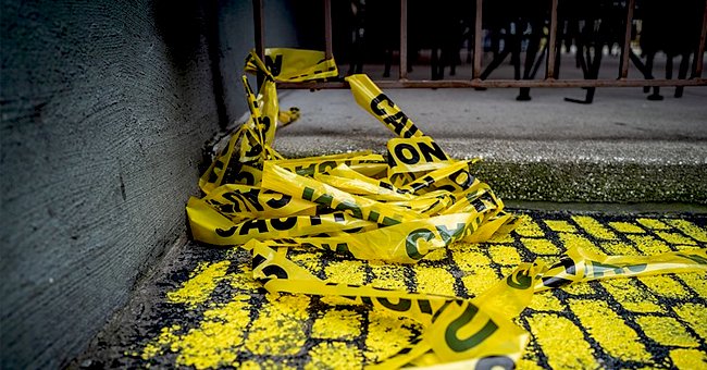 Yellow police tape lays against a gray wall and yellow painted floor. | Photo: Shutterstock