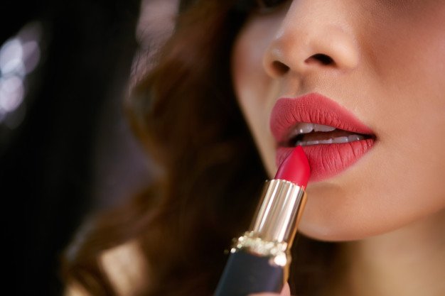 Mujer aplicando labial rojo sobre sus labios. │Foto: Freepik
