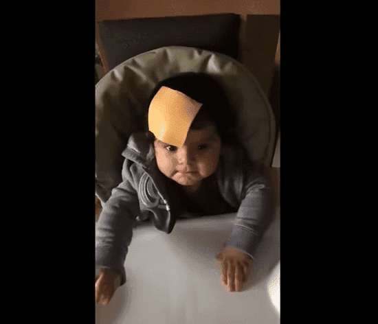 A very confused baby looks at her parents with a slice of cheese on her head | Photo: TopVids!
