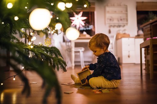 A cute toddler child sitting by Christmas tree at home | Photo: Getty Images