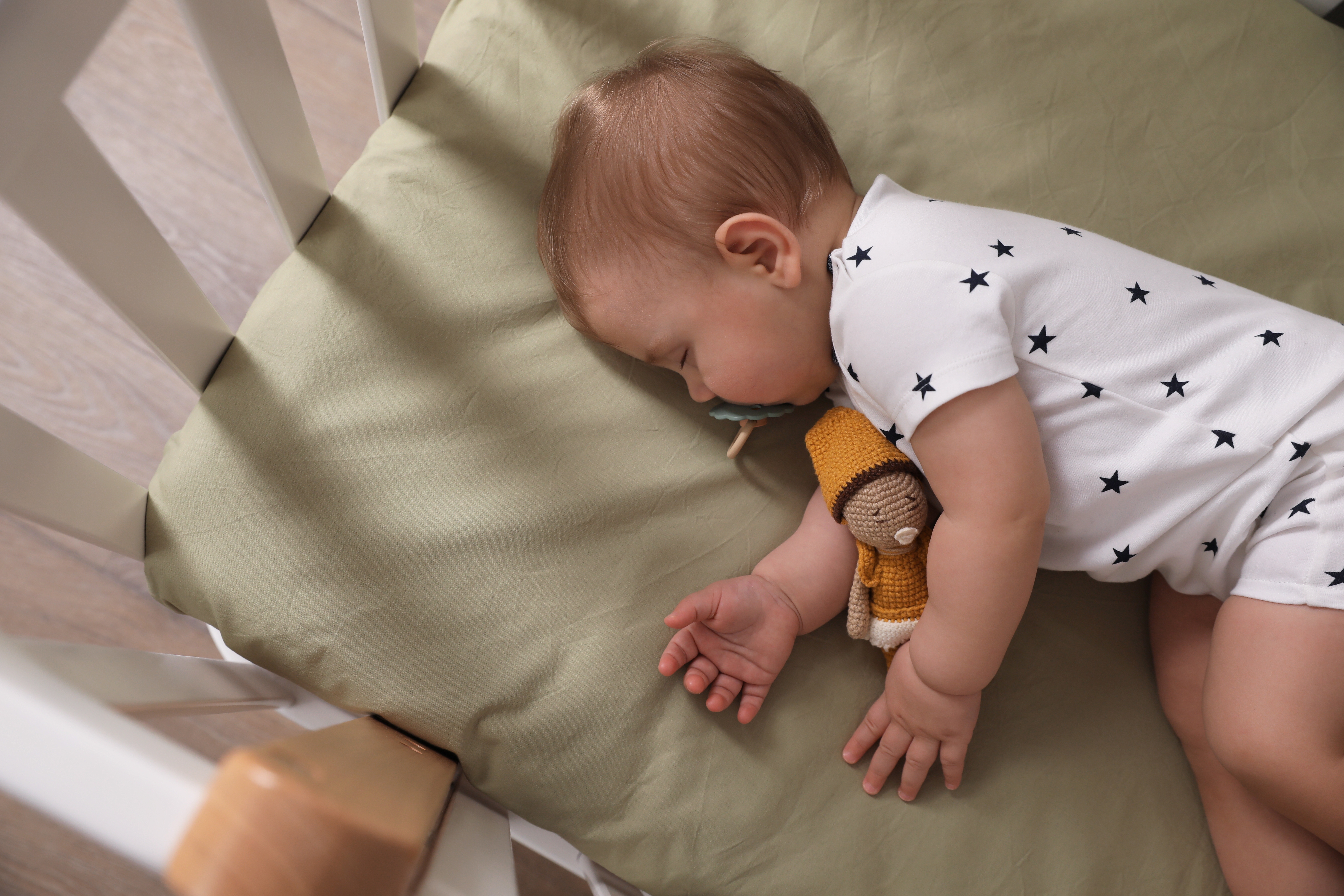 Adorable little baby with pacifier and toy sleeping in crib | Source: Shutterstock
