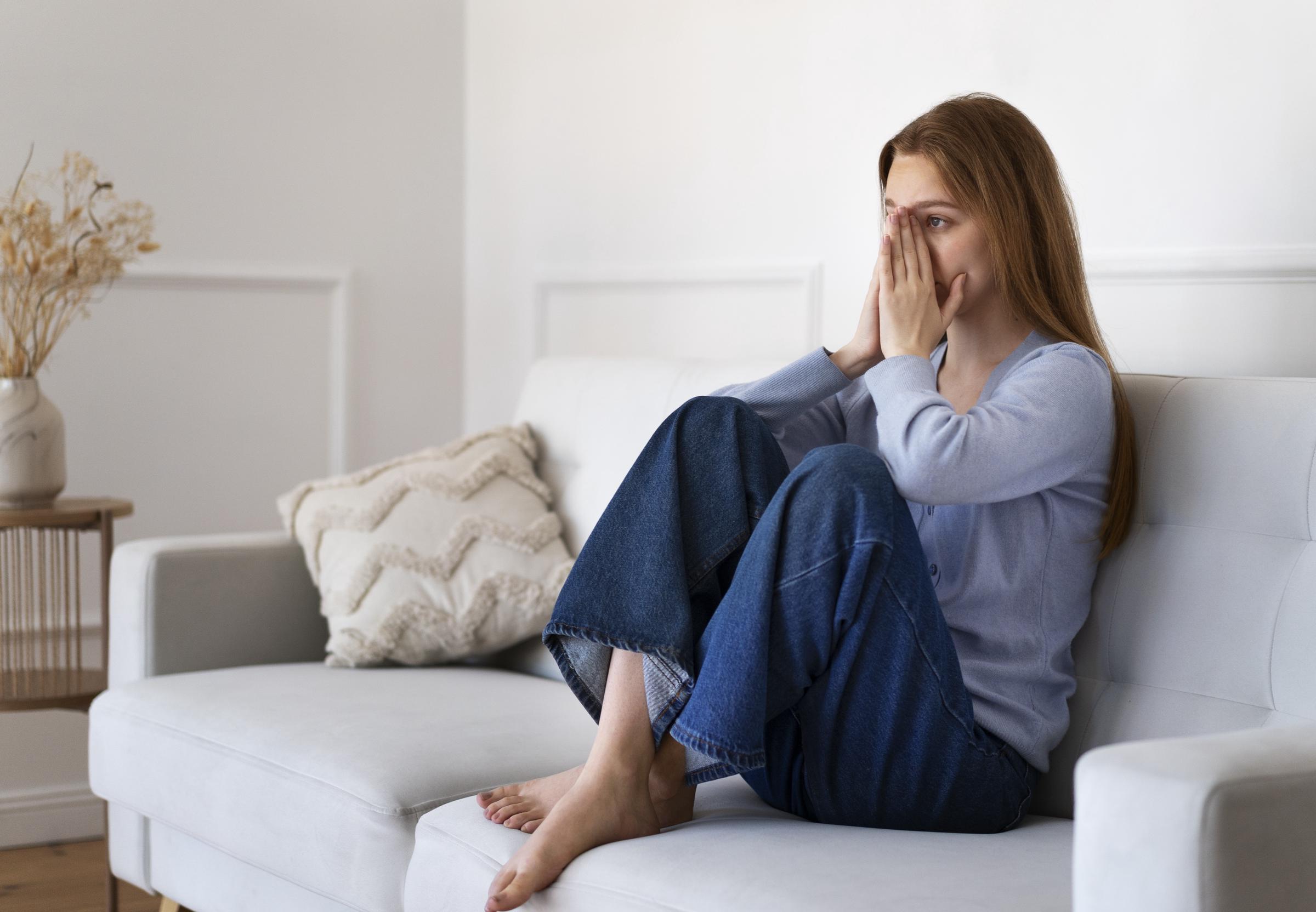 A worried woman sitting on the couch | Source: Freepik