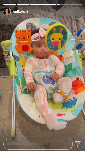 Kevin Hart's daughter, Kaori Mai, dressed in a colorful onesie and a pink bow while seated on a chair | Photo: Instagram/ enikohart
