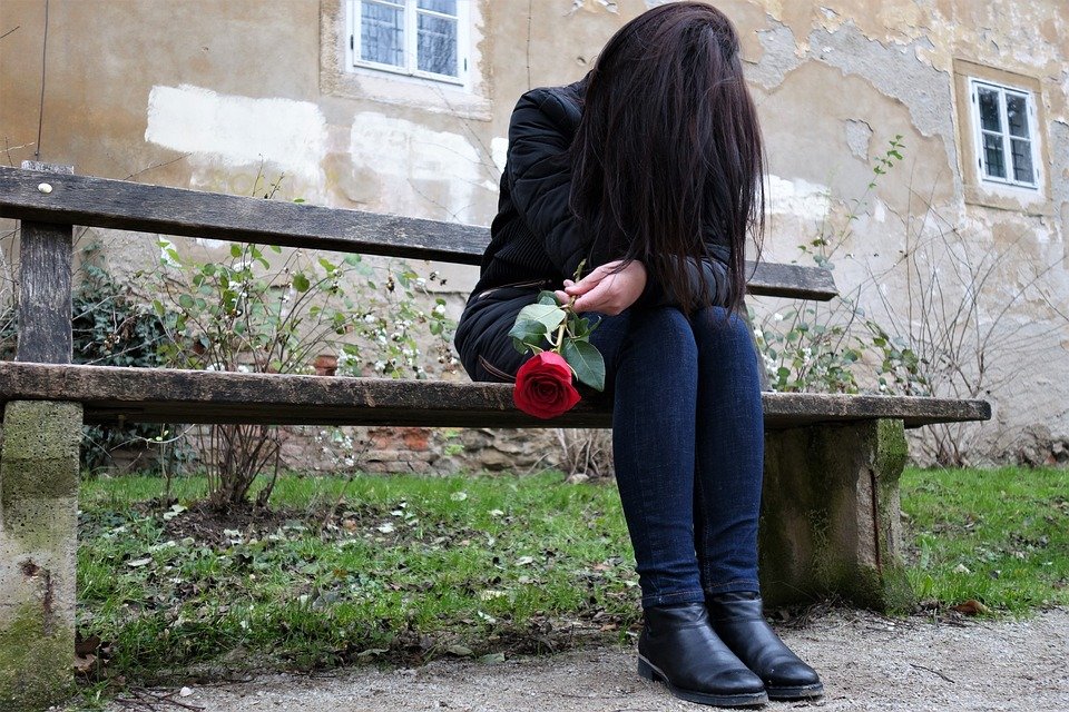 Mujer tapando su rostro con su cabello y sosteniendo una rosa con su mano. | Foto: Pixabay