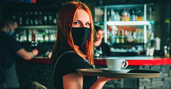 A young woman waitressing while wearing a mask. │Source: Shutterstock