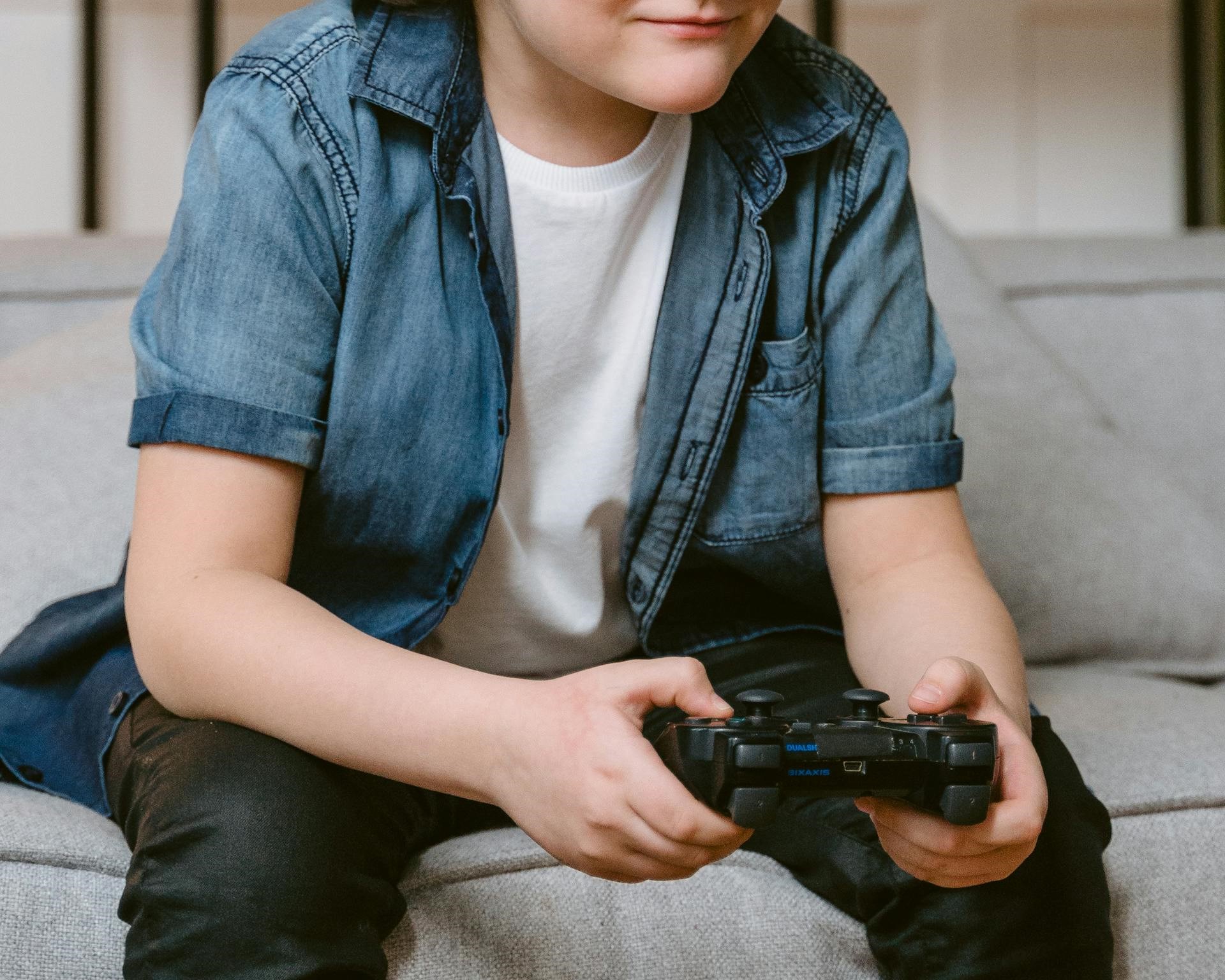 A boy sitting on the couch and holding a gaming console | Source: Pexels