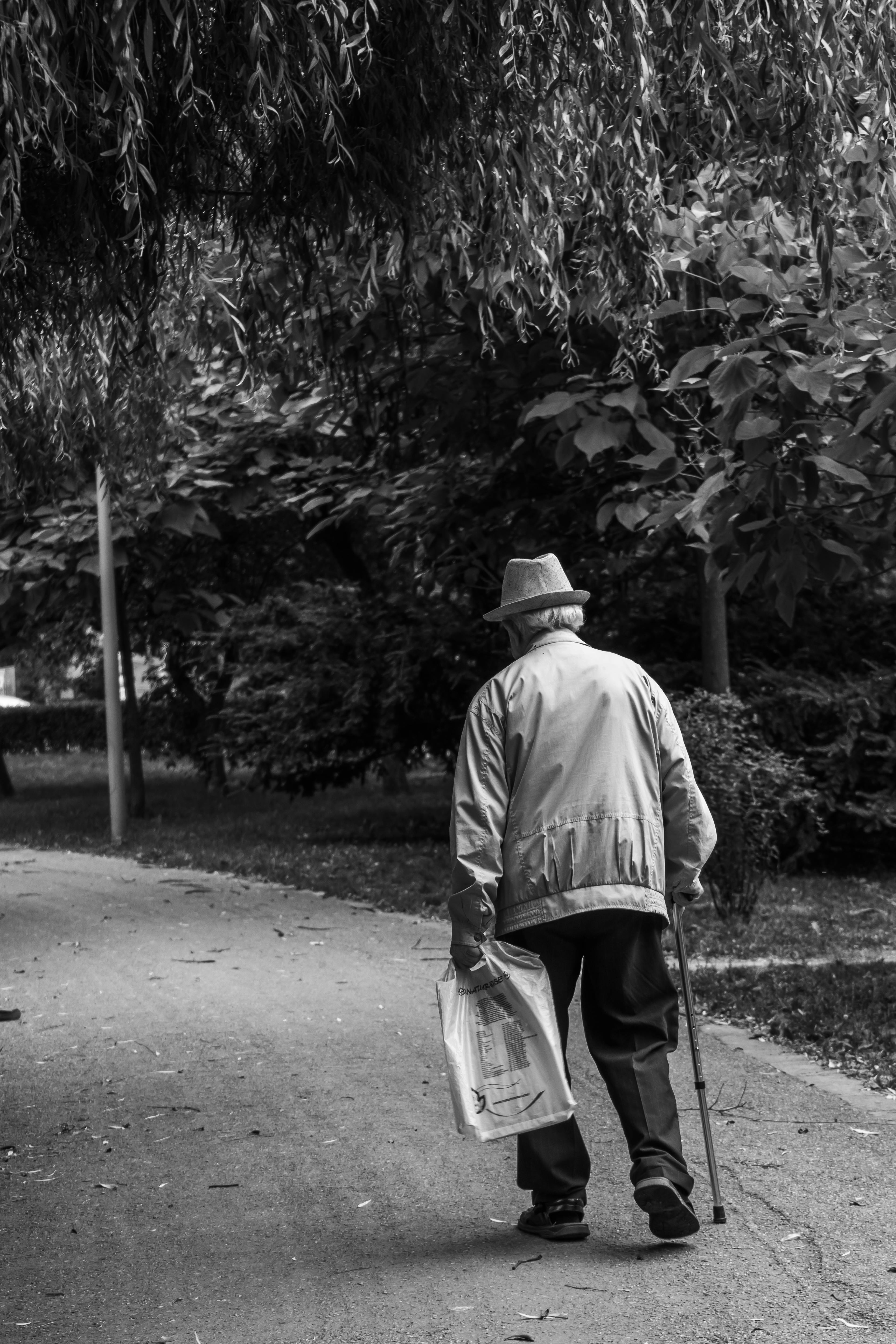 Grayscale of an old man walking with a cane and newspaper | Source: Pexels