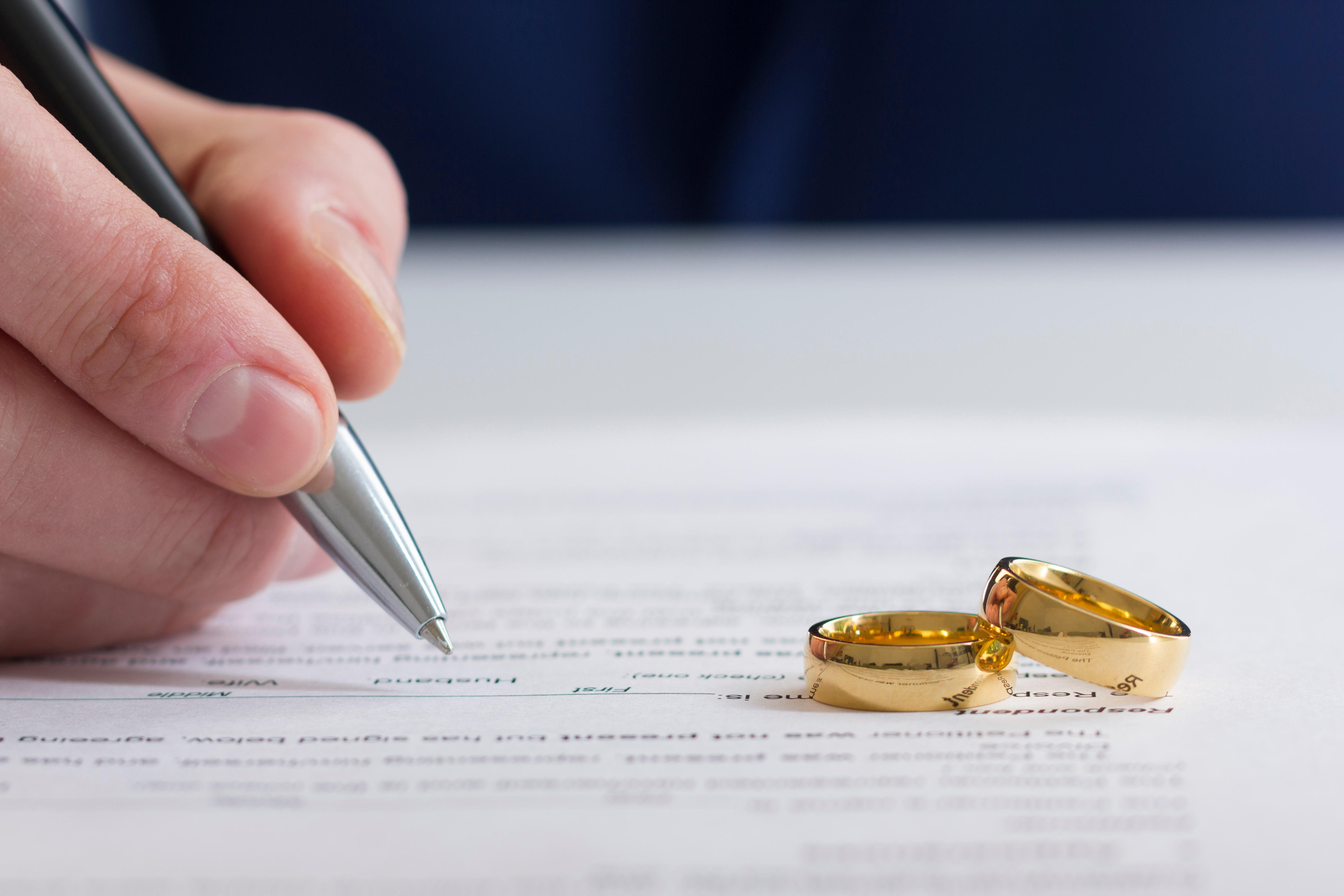A hand signing divorce papers with two rings on top | Source: Shutterstock