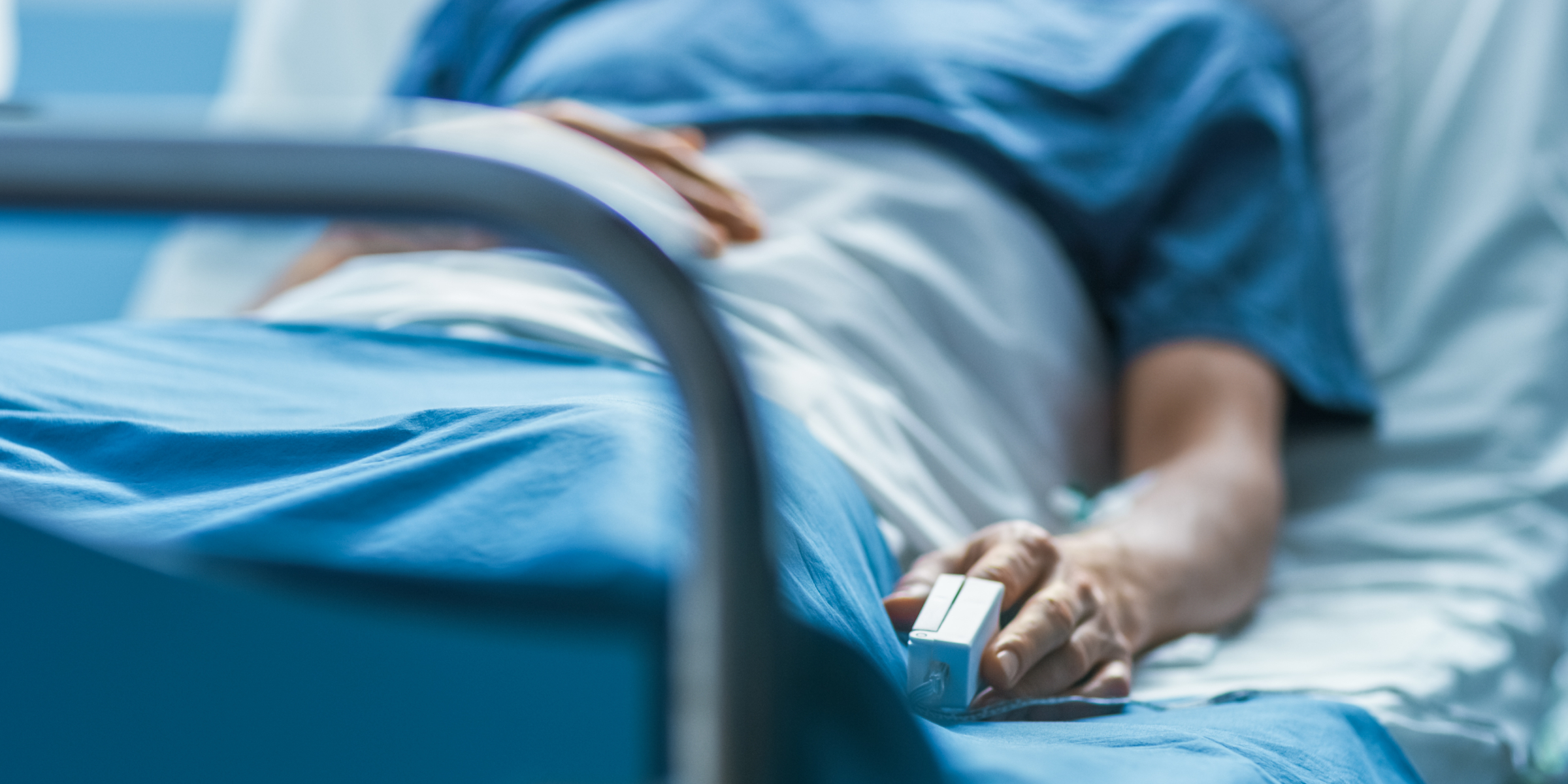 A hospital patient lies in bed wearing a pulse oximeter on their finger | Source: Getty Images