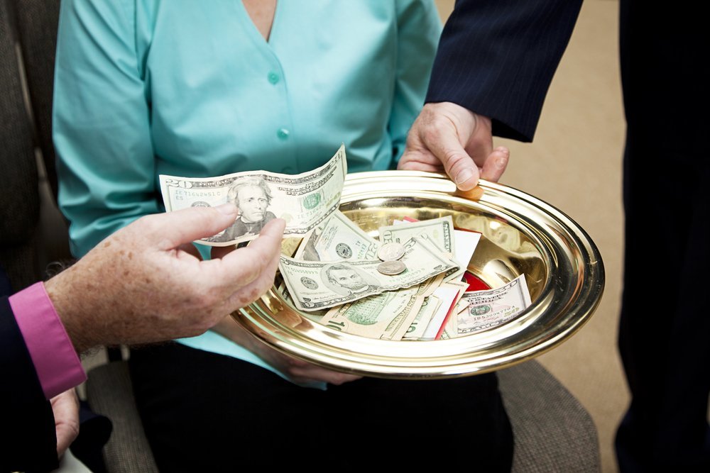 Church members putting money in the collection plate | Photo: Shutterstock