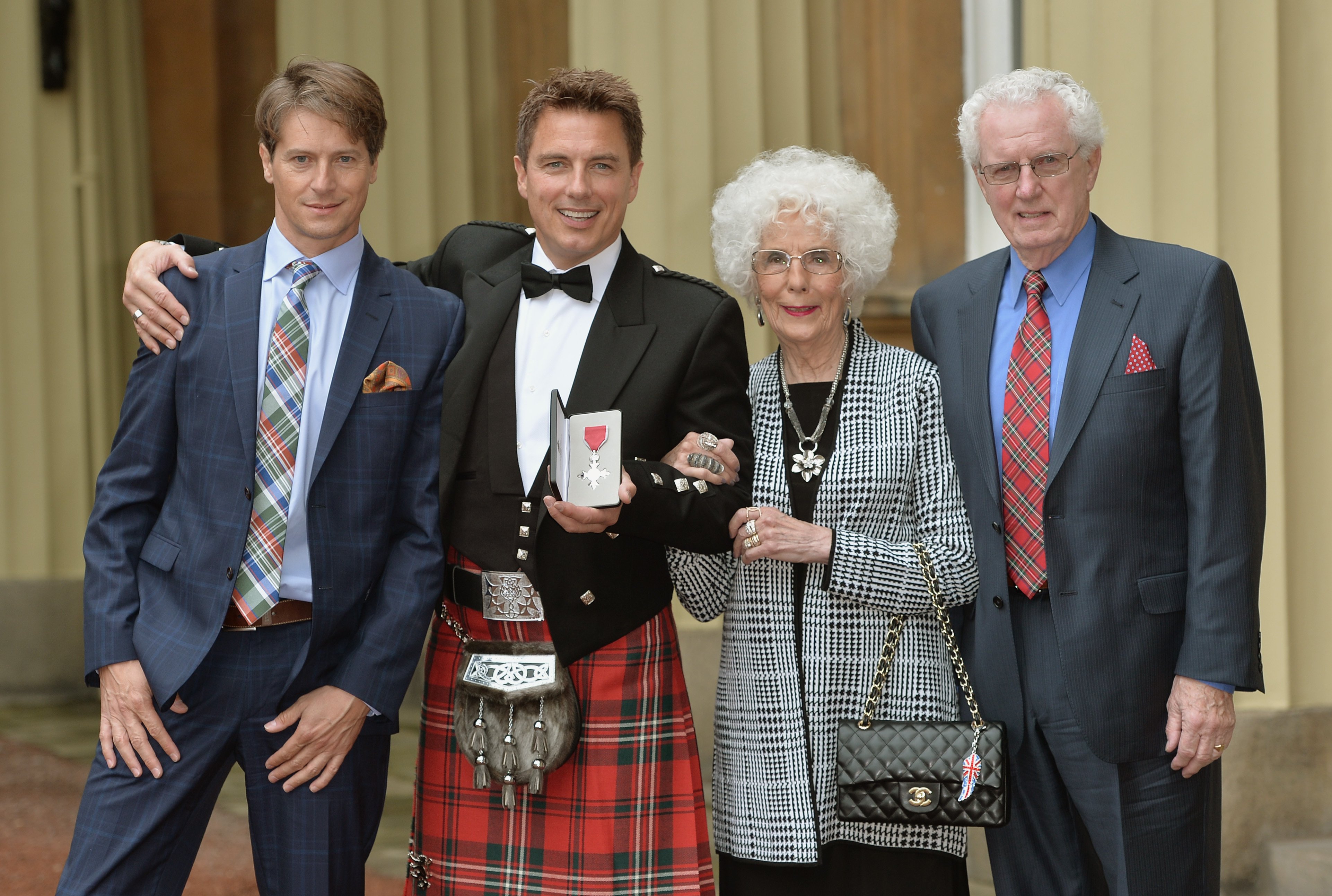 John Barrowman (2nd L) poses with husband Scott Gill (L) and parents Marion and John Barrowman after being awarded an MBE at an investiture ceremony at Buckingham Palace on October 14, 2014, in London, England. | Source: Getty Images