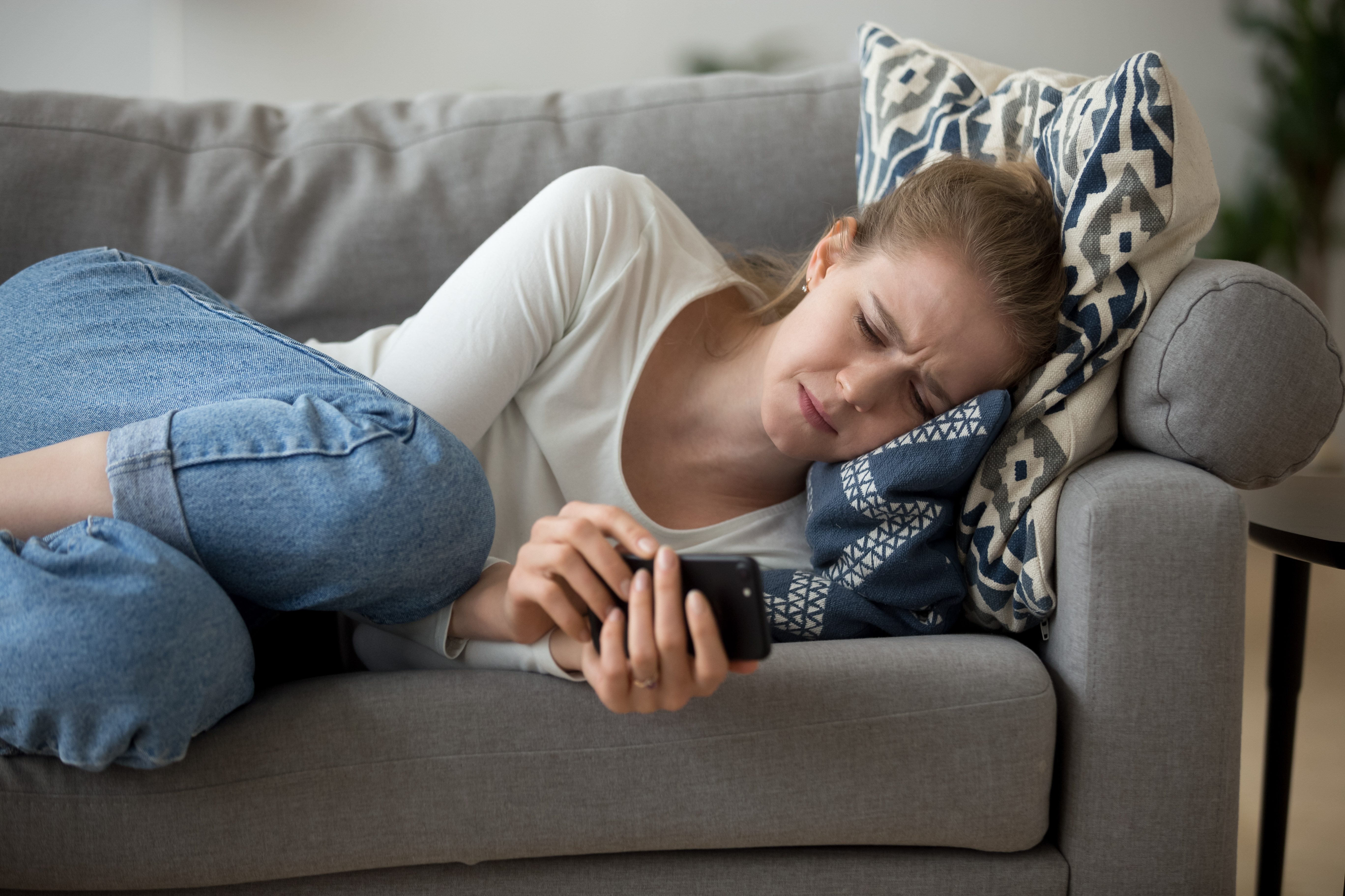 A crying woman lying on the sofa looking at her phone | Source: Shutterstock