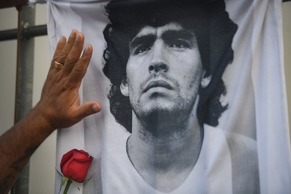 Un fan met sa main avec une rose sur un T-shirt avec la photo de la star du football Diego Maradona le jour de sa mort. |Photo : Getty Image