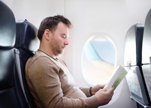 Un homme qui lit pendant son vol dans un avion | Photo : Shutterstock Un homme qui lit pendant son vol dans un avion | Photo : Shutterstock