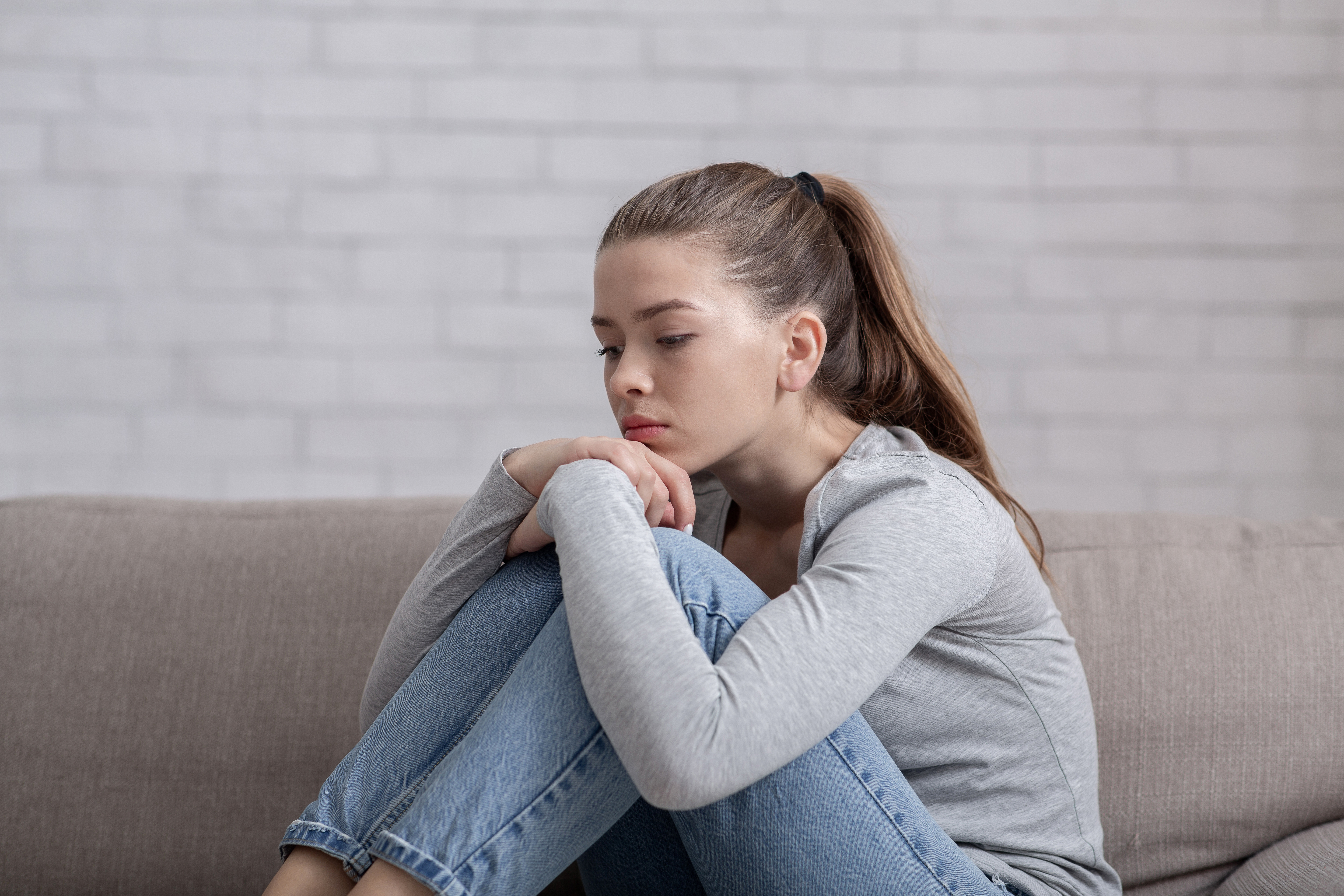 A sad young woman sitting alone on sofa | Source: Shutterstock
