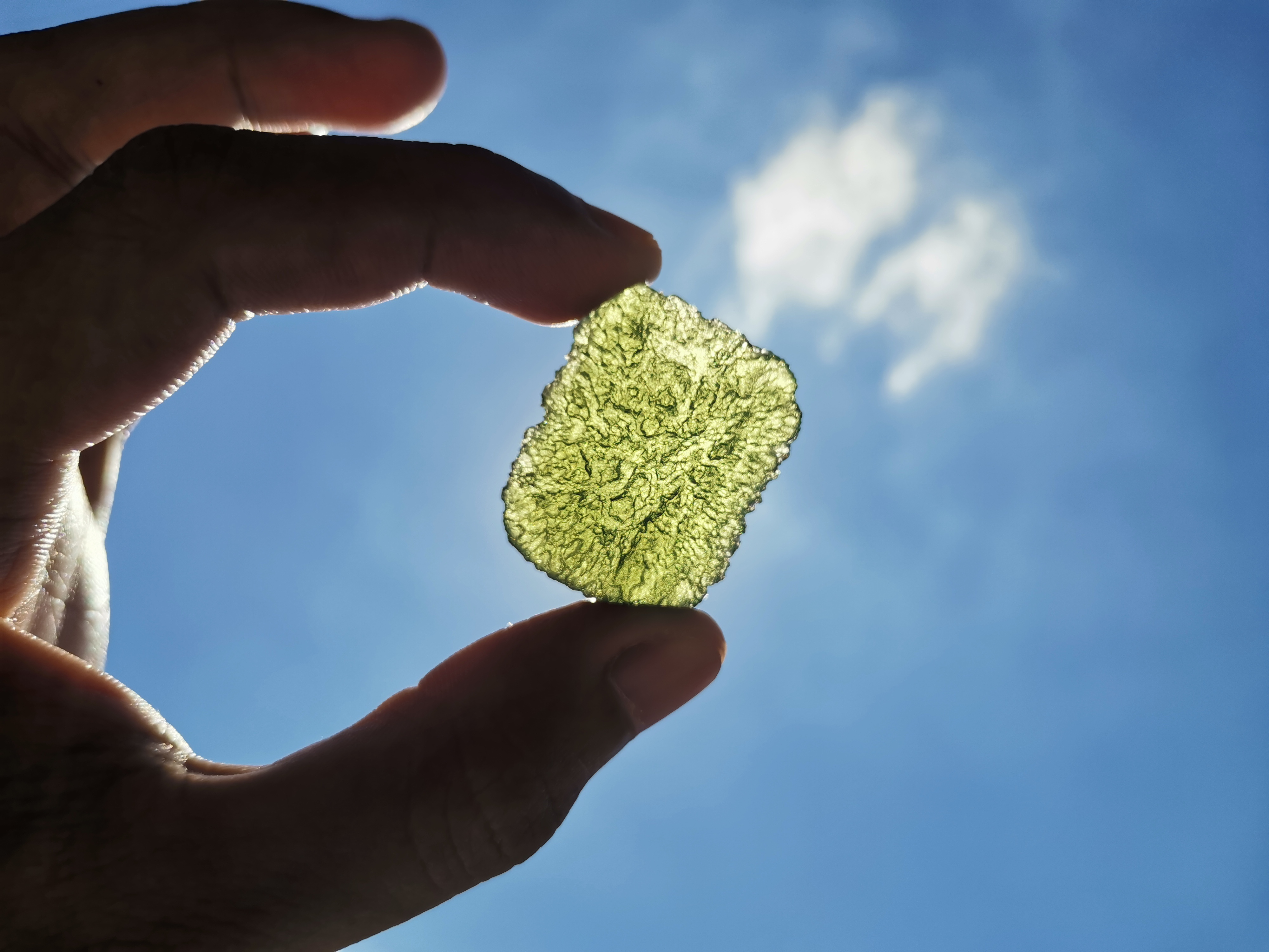 Photo of someone holding a piece of moldavite in the sun | Source: Getty Images