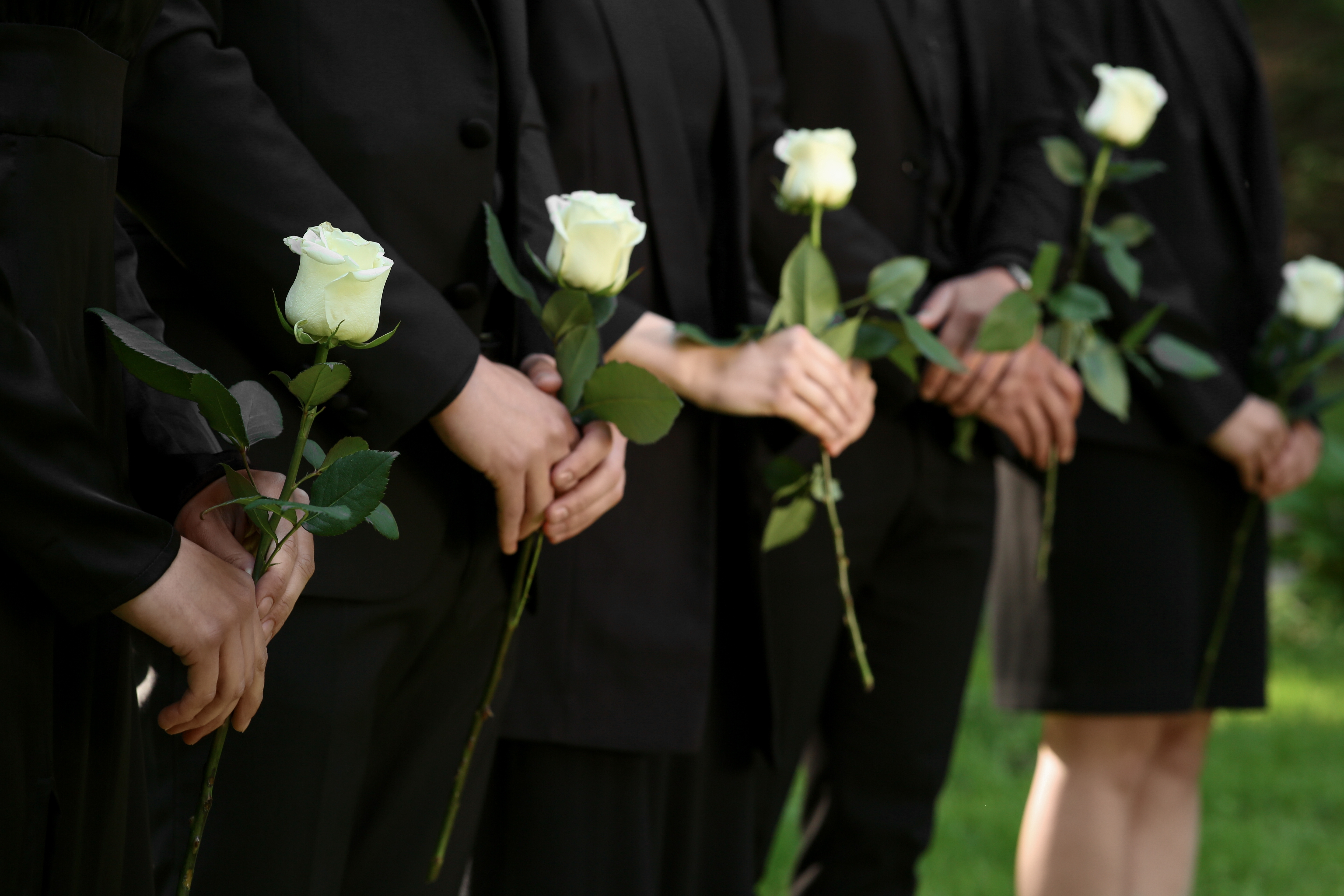 People in black clothes with white rose flowers outdoors, closeup. Funeral ceremony. | Source: Shutterstock