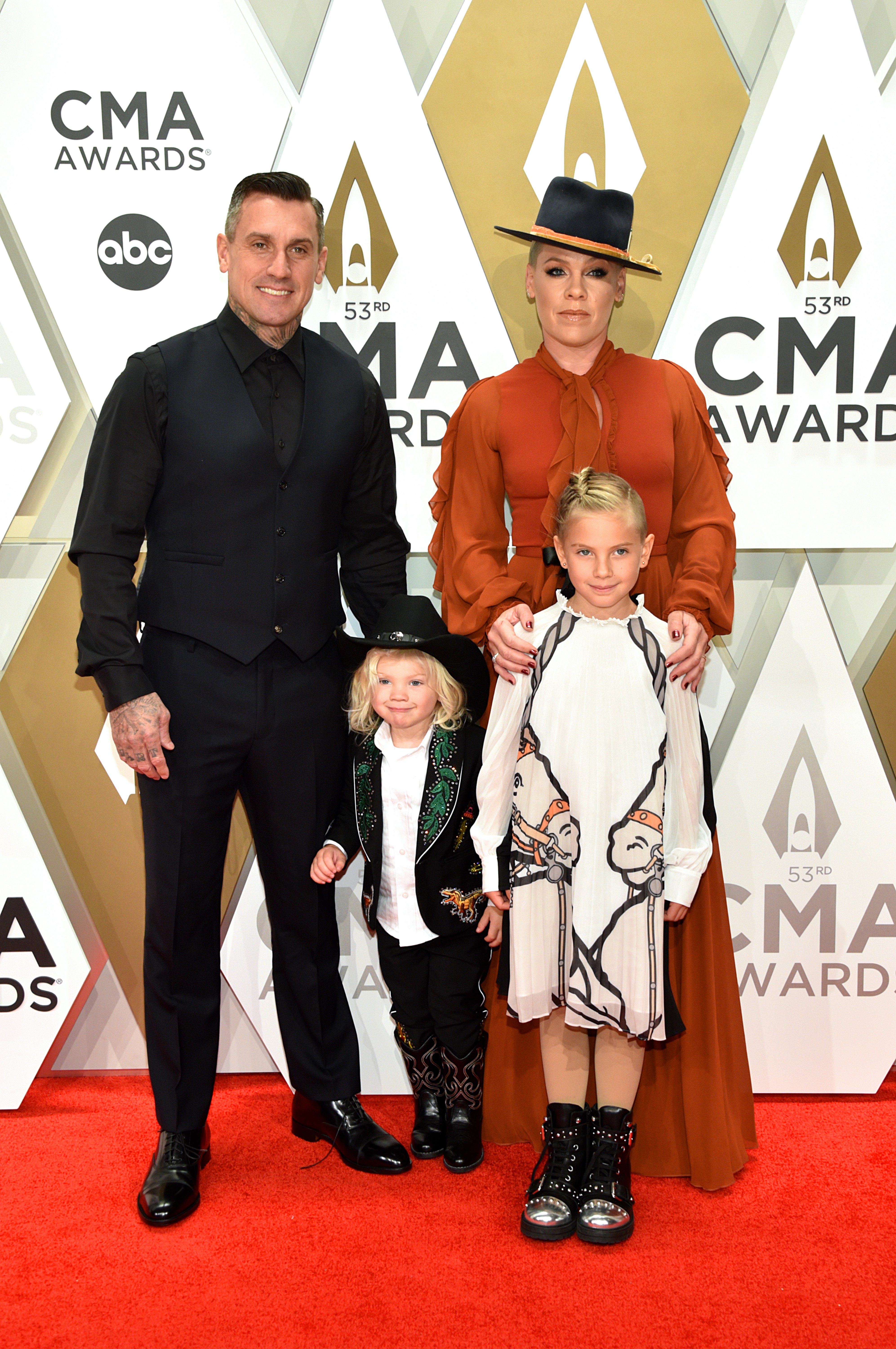 Carey Hart, Jameson Moon Hart, Willow Sage Hart, and Pink pose at the 53rd Annual CMA Awards on November 13. Pink stands in a rust-colored gown and hat, with Willow front and center in a white dress.
