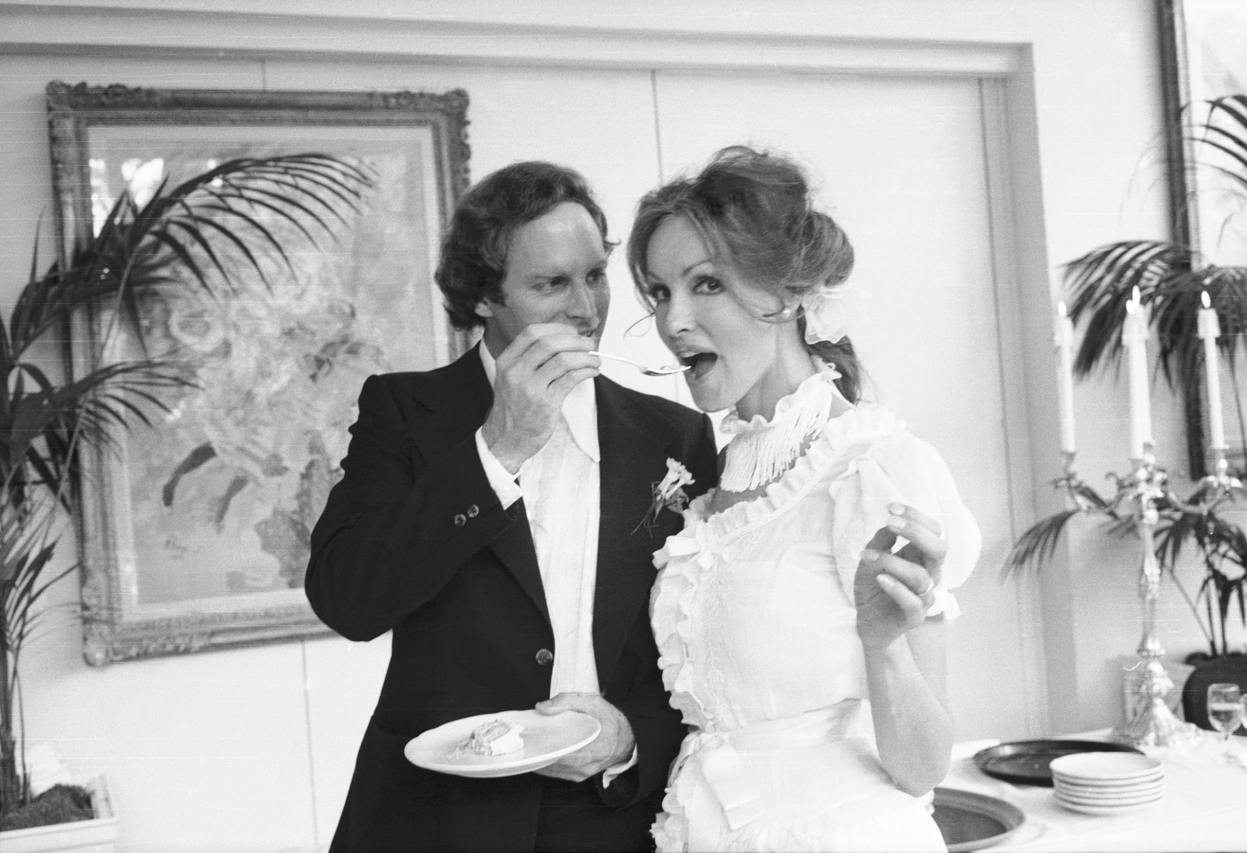 American actress Julie Newmar looks to the camera as lawyer J. Holt Smith feeds her cake at the reception following their wedding, New York, New York, August 5, 1977. | Source: Getty Images