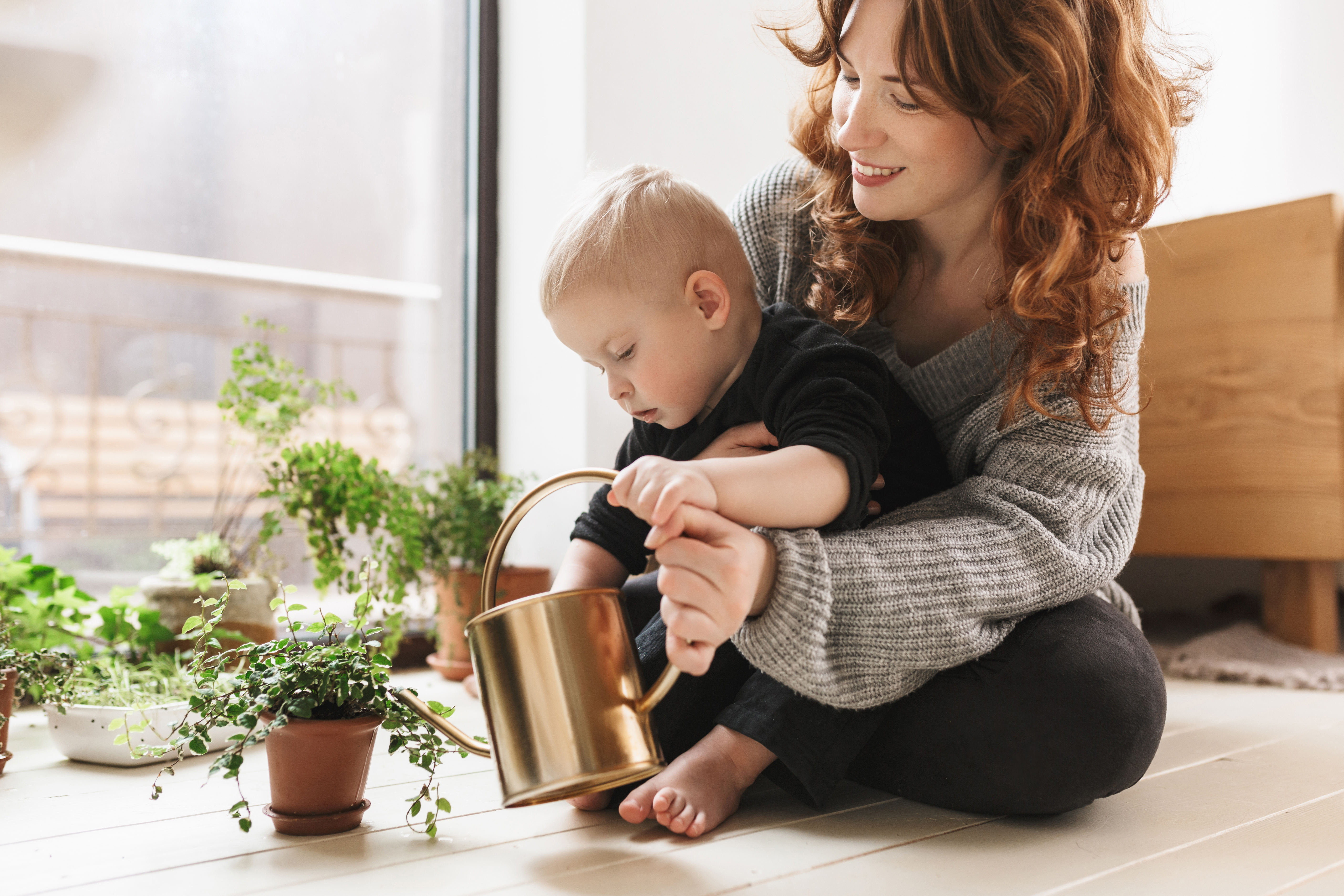 A woman teaching her baby how to water the plants | Source: Shutterstock