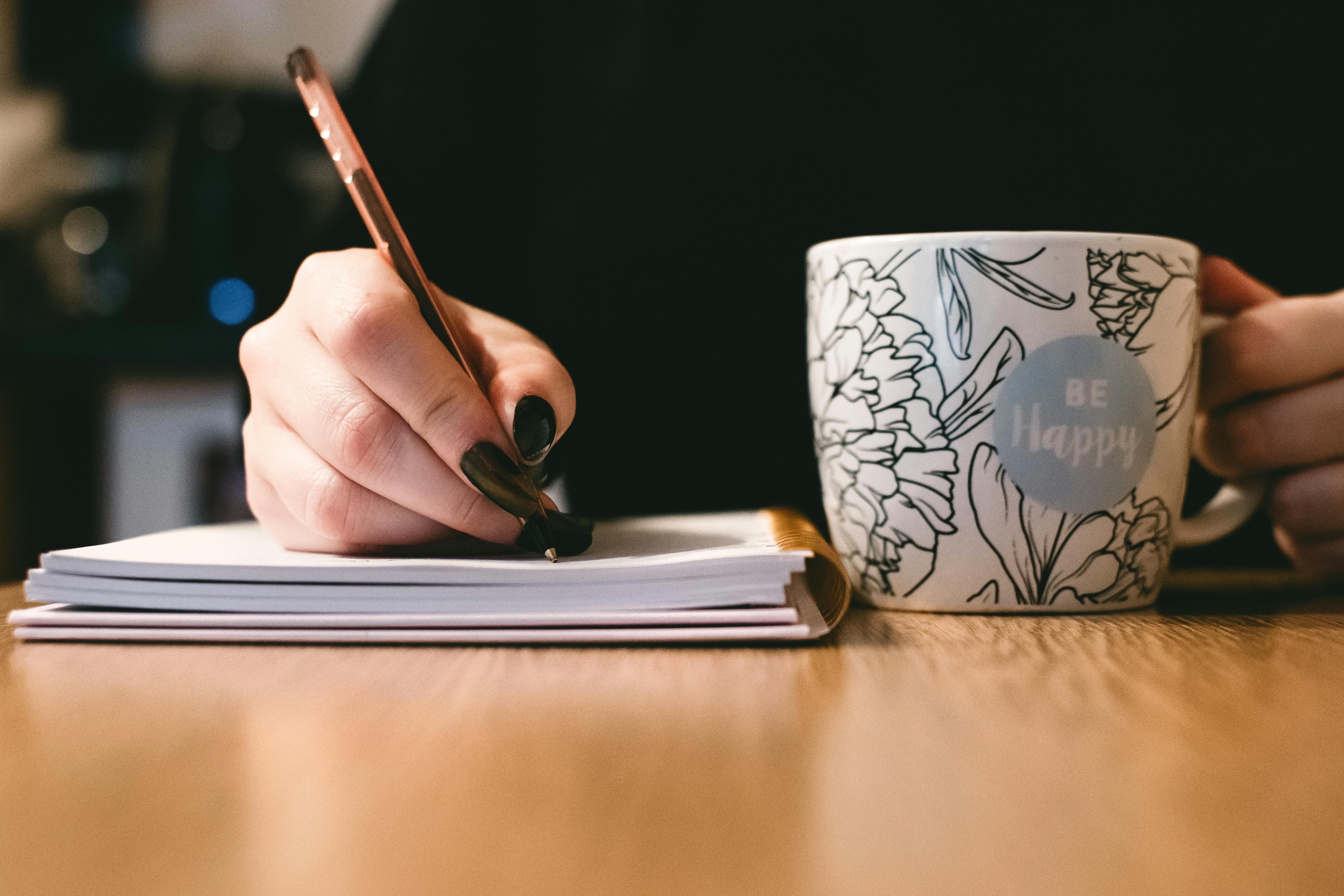 A woman writing on a notepad with a cup of coffee nearby | Source: Pexels