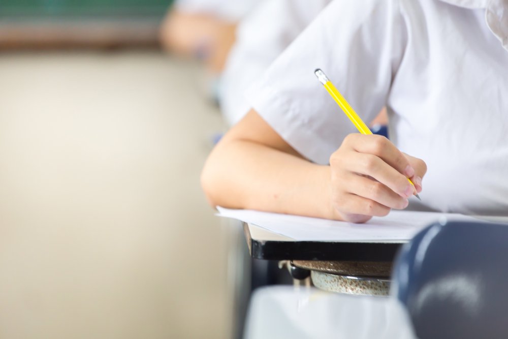 Student holding pencil and writing on paper answer sheet during an examination. | Photo: Shutterstock