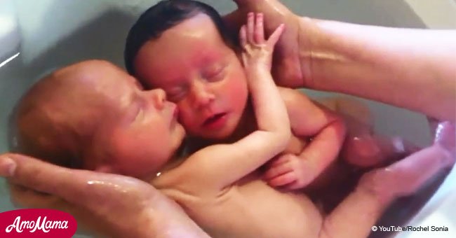 Newborn twins relaxing in a bath won't stop hugging each other