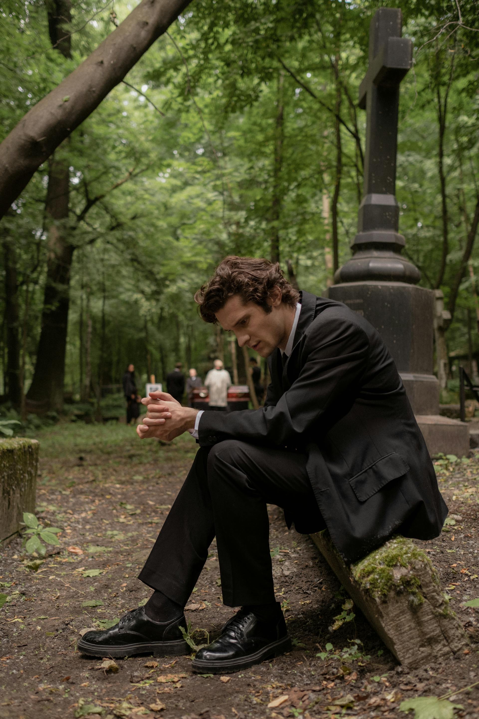 A man in a black suit and jacket sitting in a cemetery | Source: Pexels