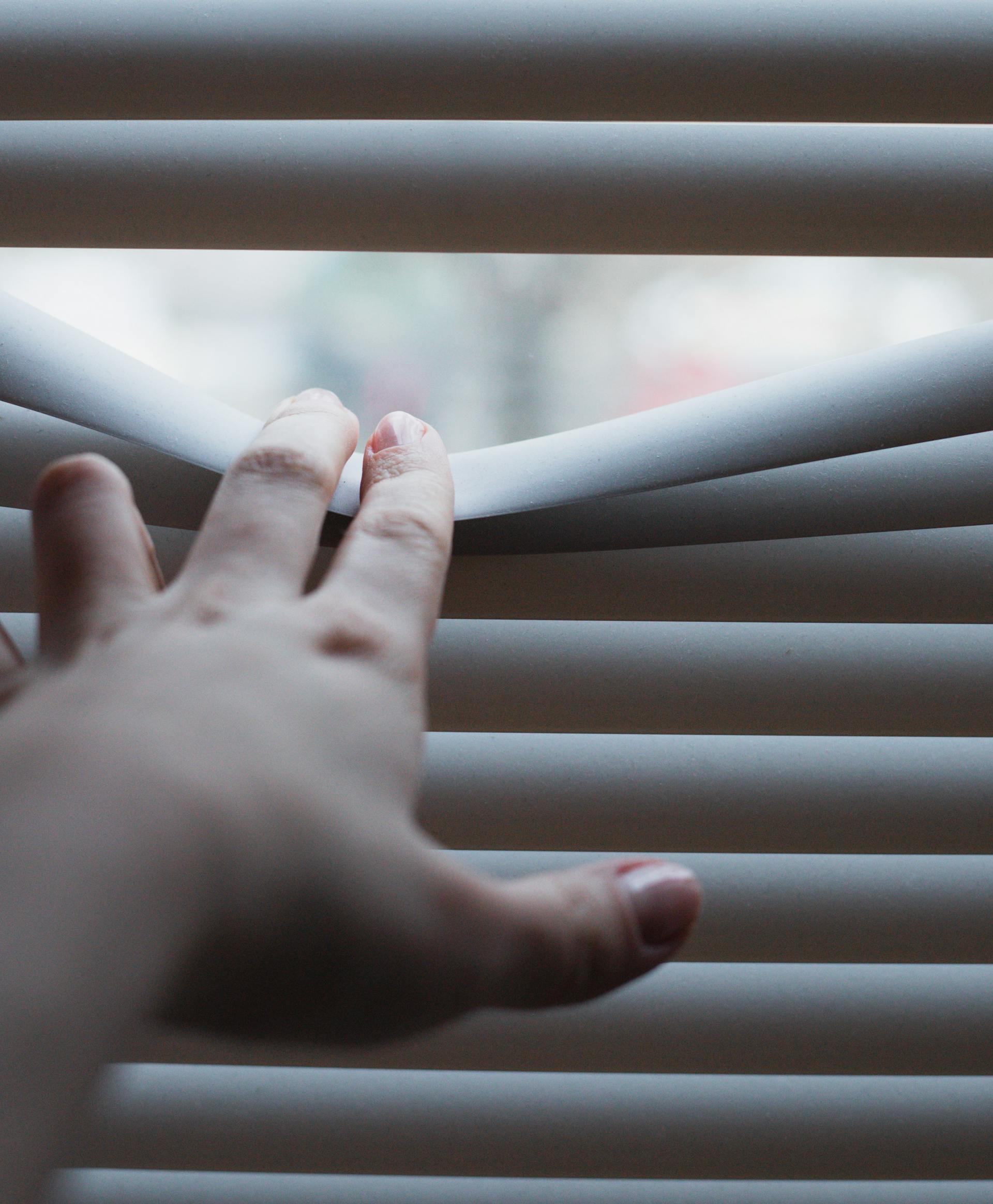 A person's hand on window blinds | Source: Pexels