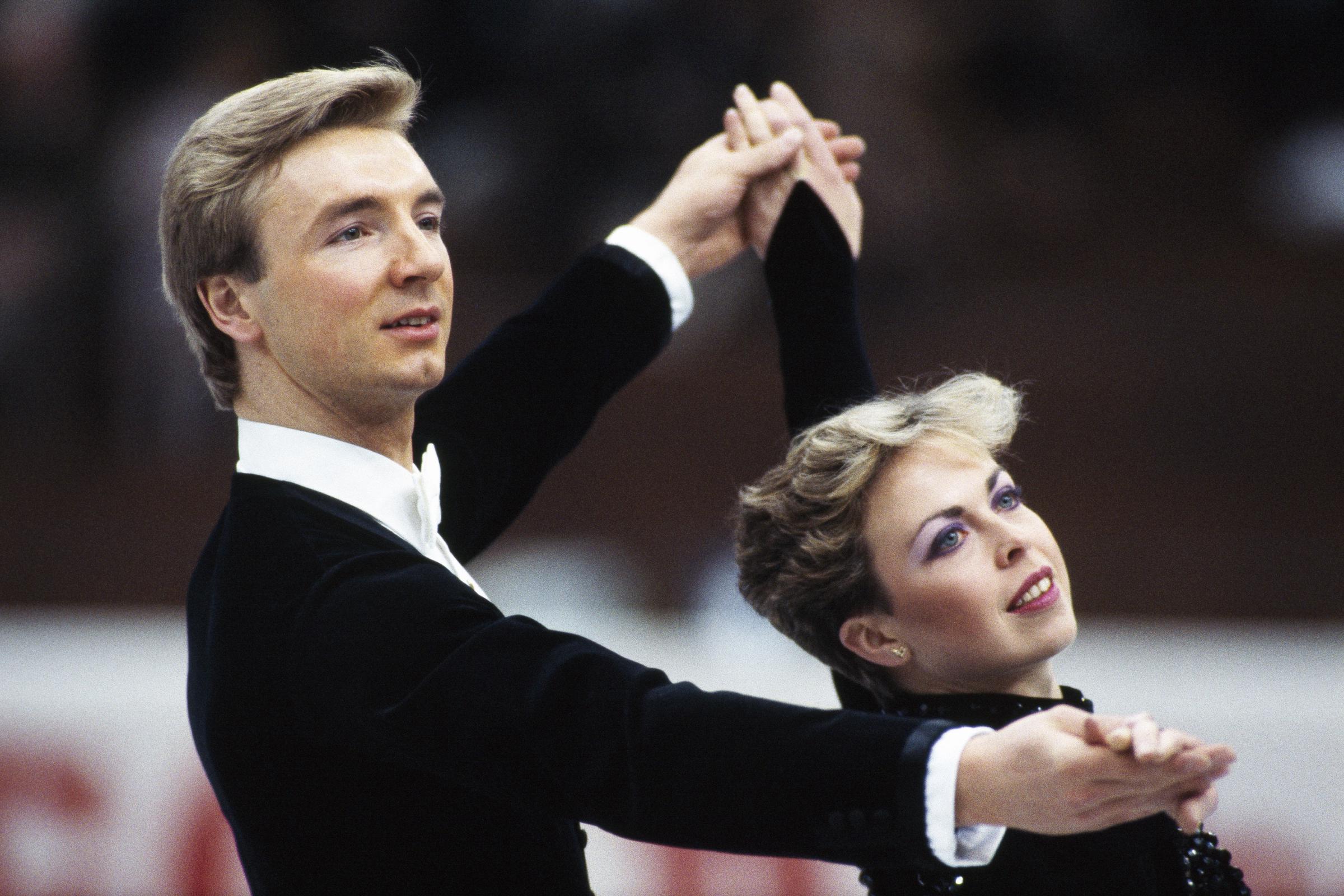 Torvill and Dean hold a poised ballroom-style position during their Olympic-winning era. With arms lifted and hands linked, they glide in elegant synchrony, their lines crisp and controlled.