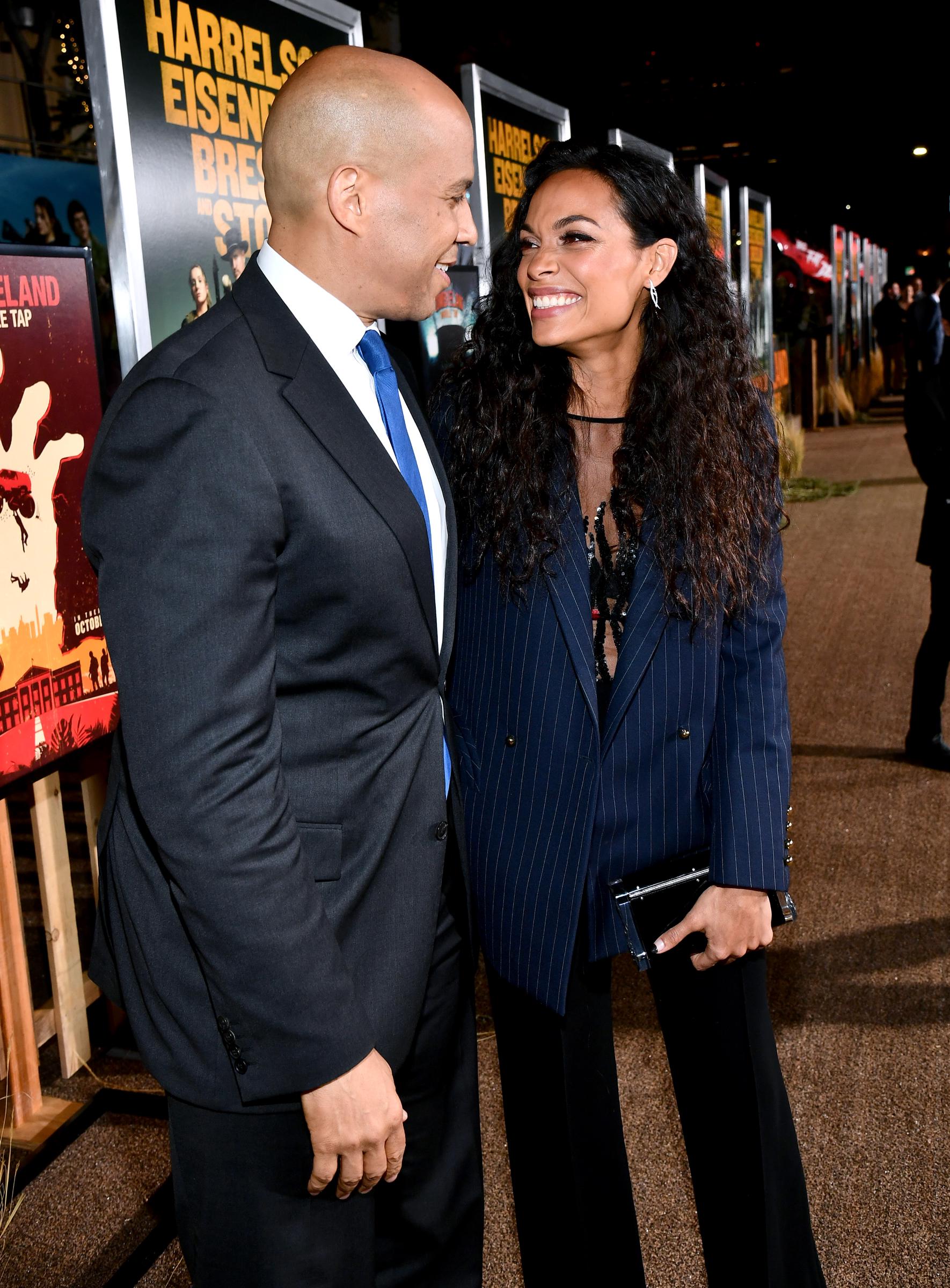 Rosario Dawson looks up at Cory Booker with a wide smile as they share a candid laugh. Their relaxed energy and close connection light up the carpet in an otherwise formal setting.