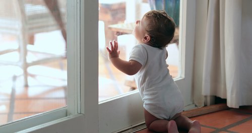 Un bébé qui s'appuie sur la fenêtre | Photo : Shutterstock