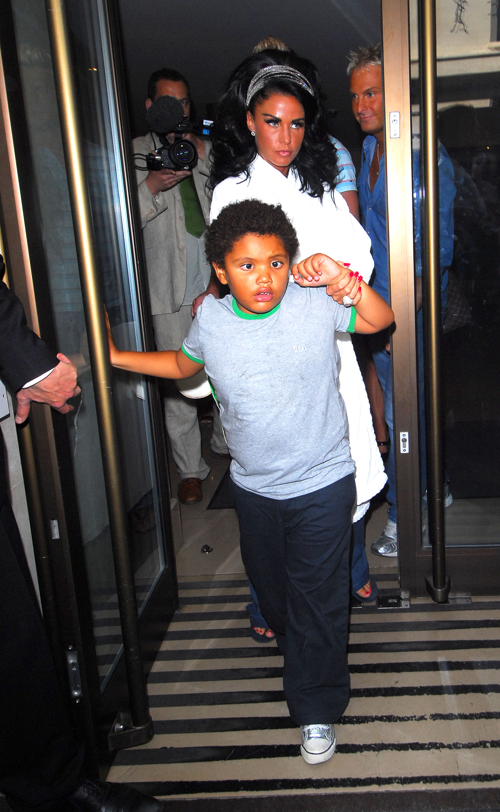 Katie Price is seen guiding her son, Harvey Price, out of their hotel on August 9, 2009, in London, as the pair head to the wedding of friends Phil Turner and Gary Cockerill. Dressed casually and clutching her hand, Harvey appeared wary of the media attention, while Katie remained composed amid the flashing cameras and press awaiting their arrival.