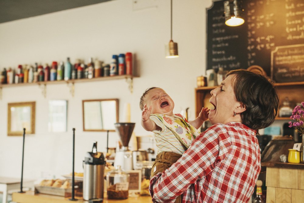 A woman holding a crying baby in a coffee shop. | Photo: Shutterstock.