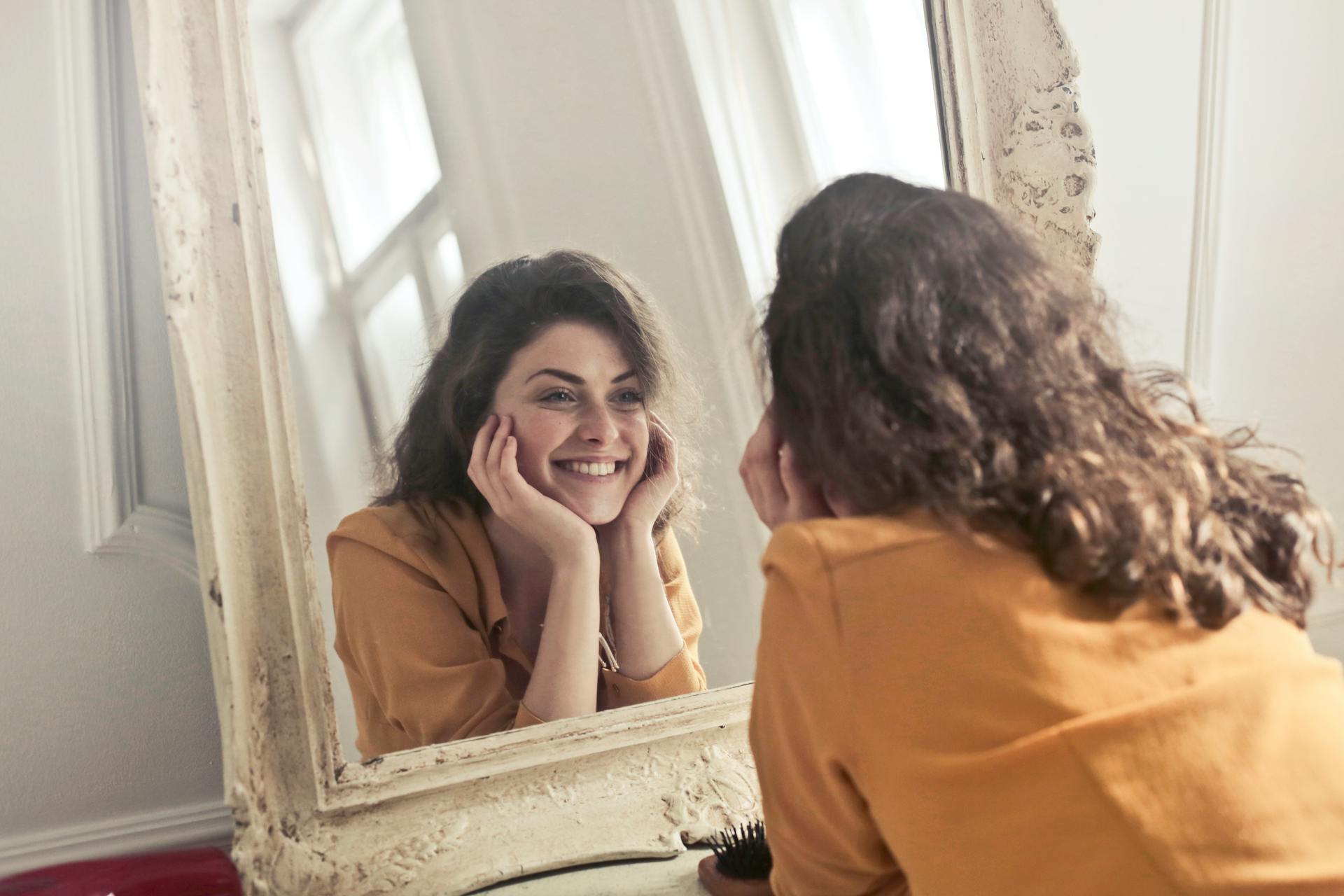 A smiling woman looking at her reflection in the mirror | Source: Pexels