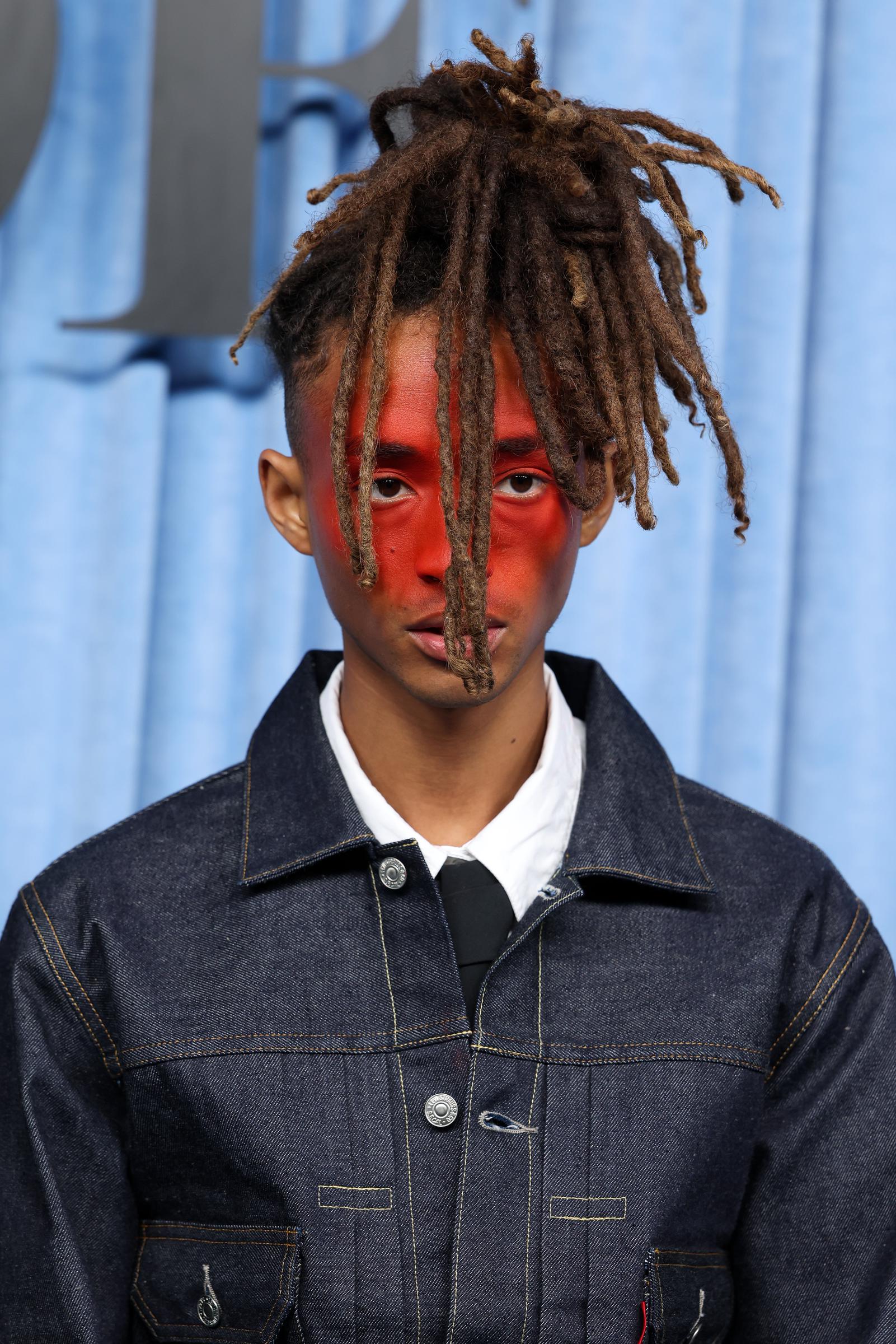 Jaden Smith attended the BoF500 Gala during Paris Fashion Week in France. His shoulder-length brown dreadlocks paired with a shaved undercut was styled in an updo, and he wore distinctive makeup that made the center of his face appear red. In a close-up shot, he gazes ahead with a striking, model-like pose.
