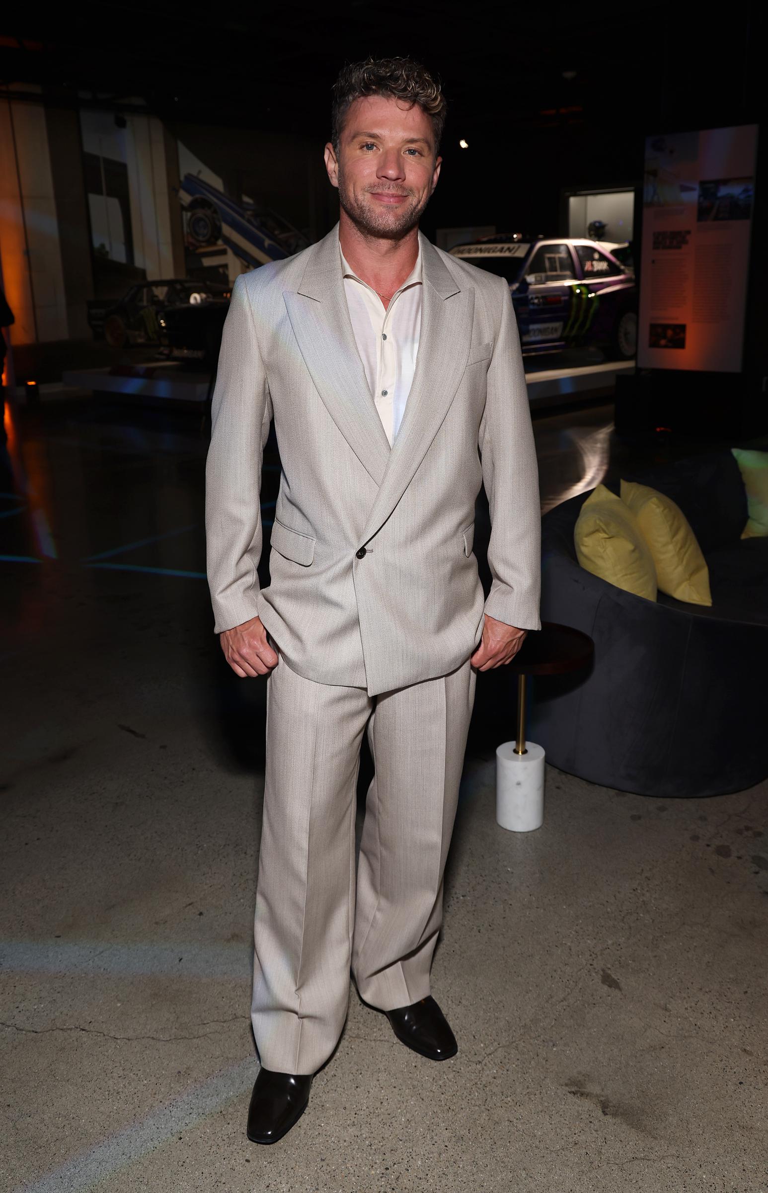 Inside the Academy Museum, Ryan Phillippe is seen in a softly lit setting at the "Motorheads" screening, wearing his light beige suit while casually posing amid the vintage cars and ambient lighting of the event space.