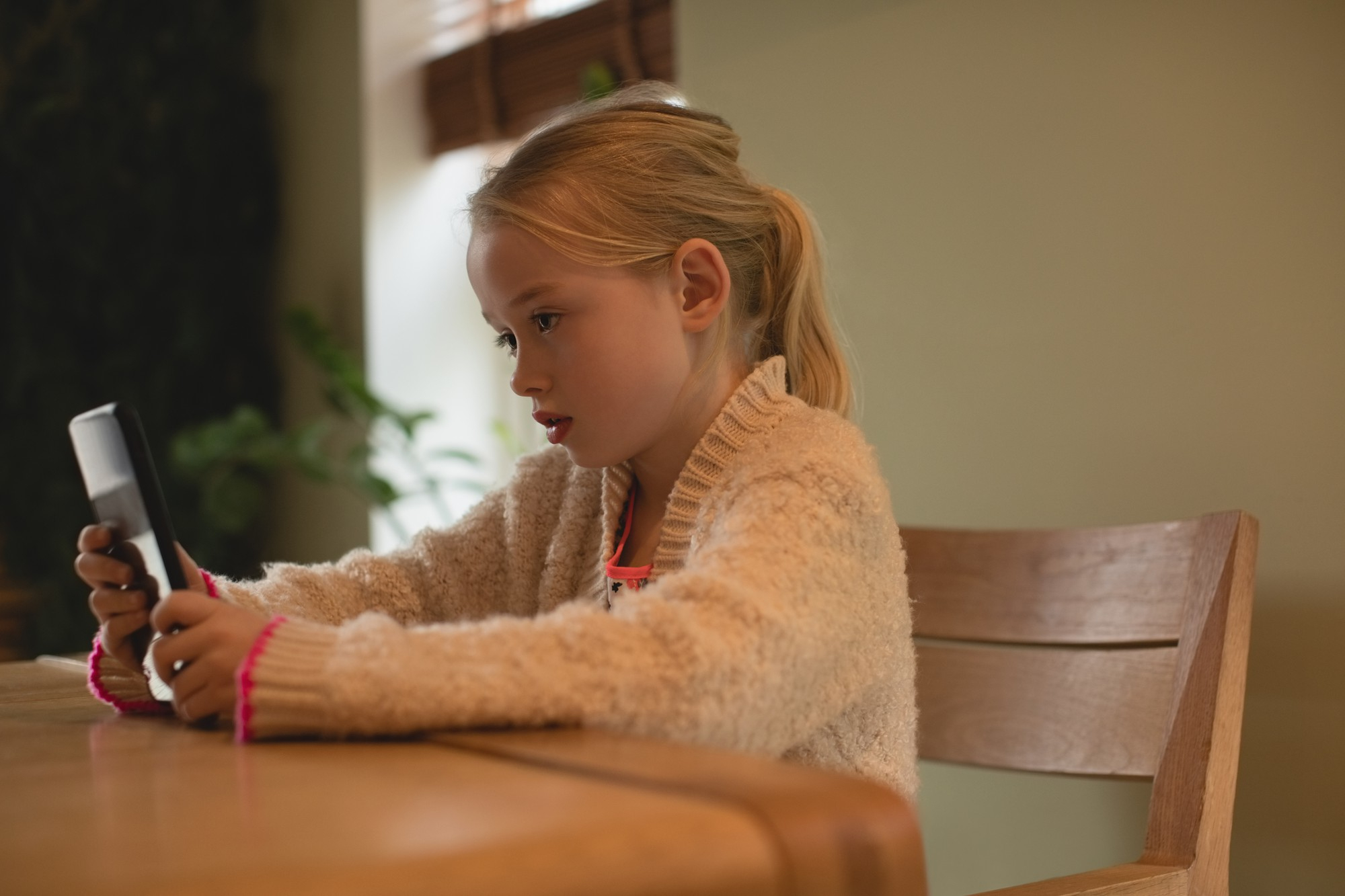 A little girl using a phone while seated at a table | Source: Freepik