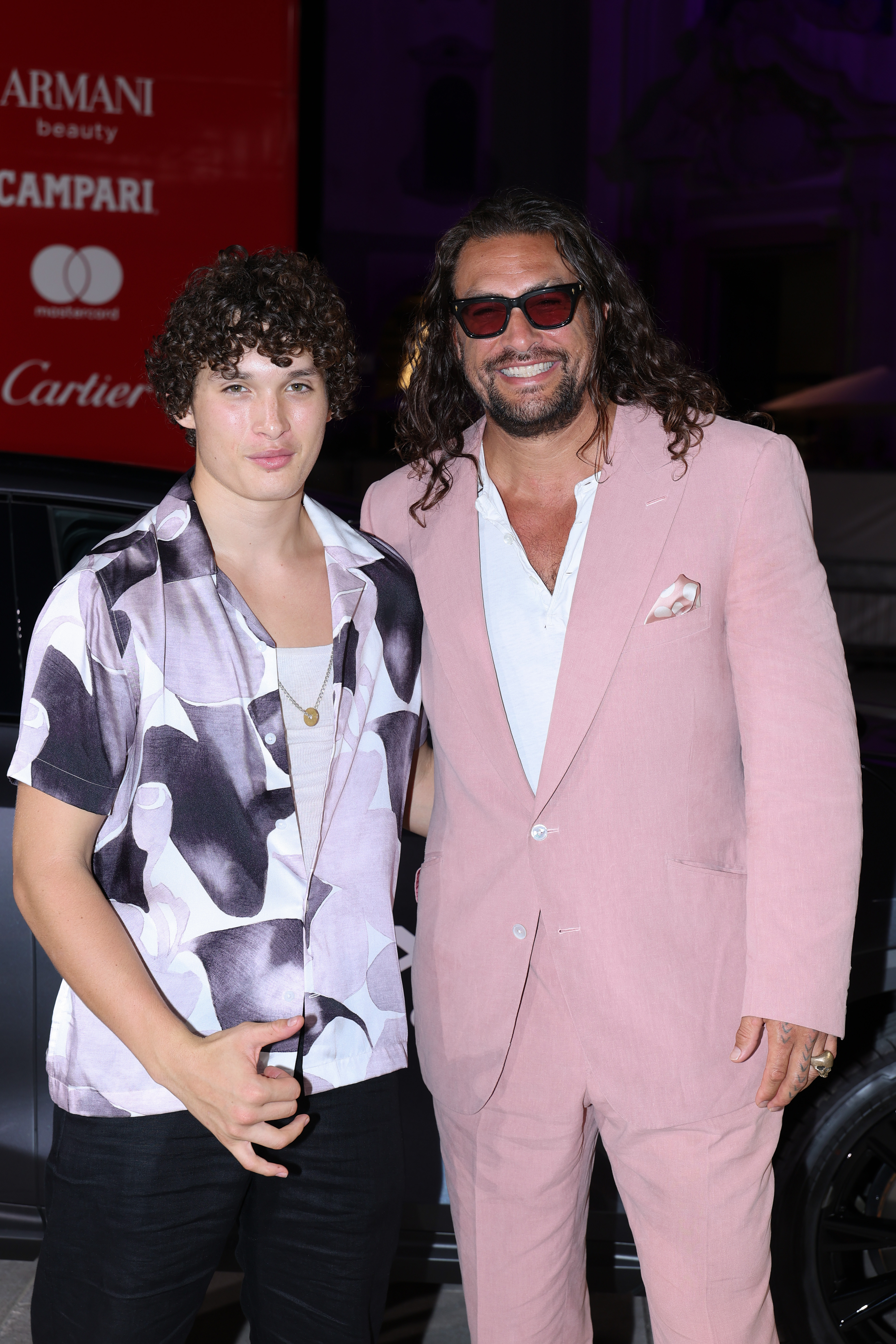 Nakoa-Wolf Momoa lifted his hand mid-gesture as he posed beside Jason Momoa outside the "In the Hand of Dante" screening, adding a playful touch to their composed father-son moment at the Venice Film Festival.