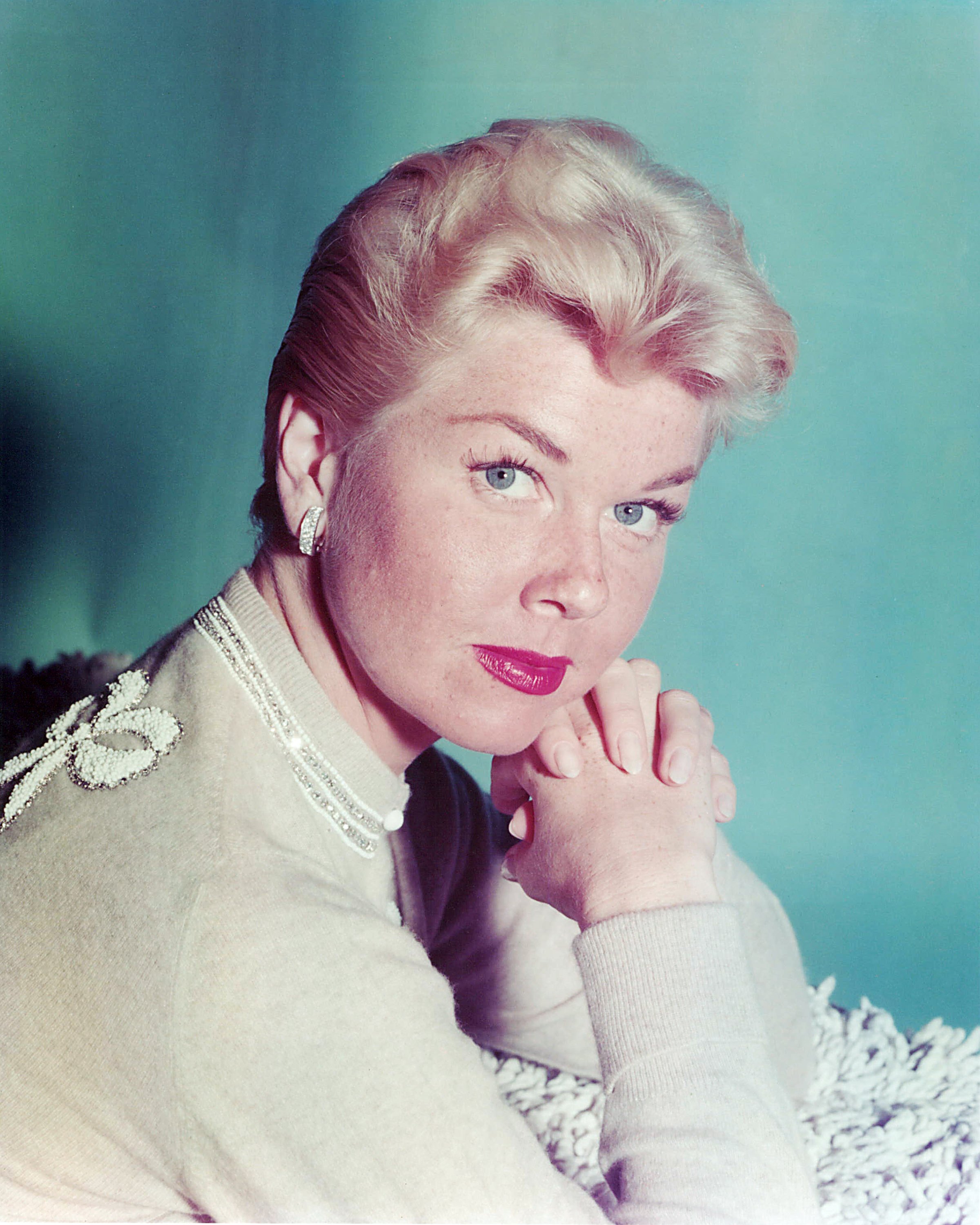 Doris Day wearing a jumper, posing with her hands clasped together against a light blue background in 1955. / Source: Getty Images