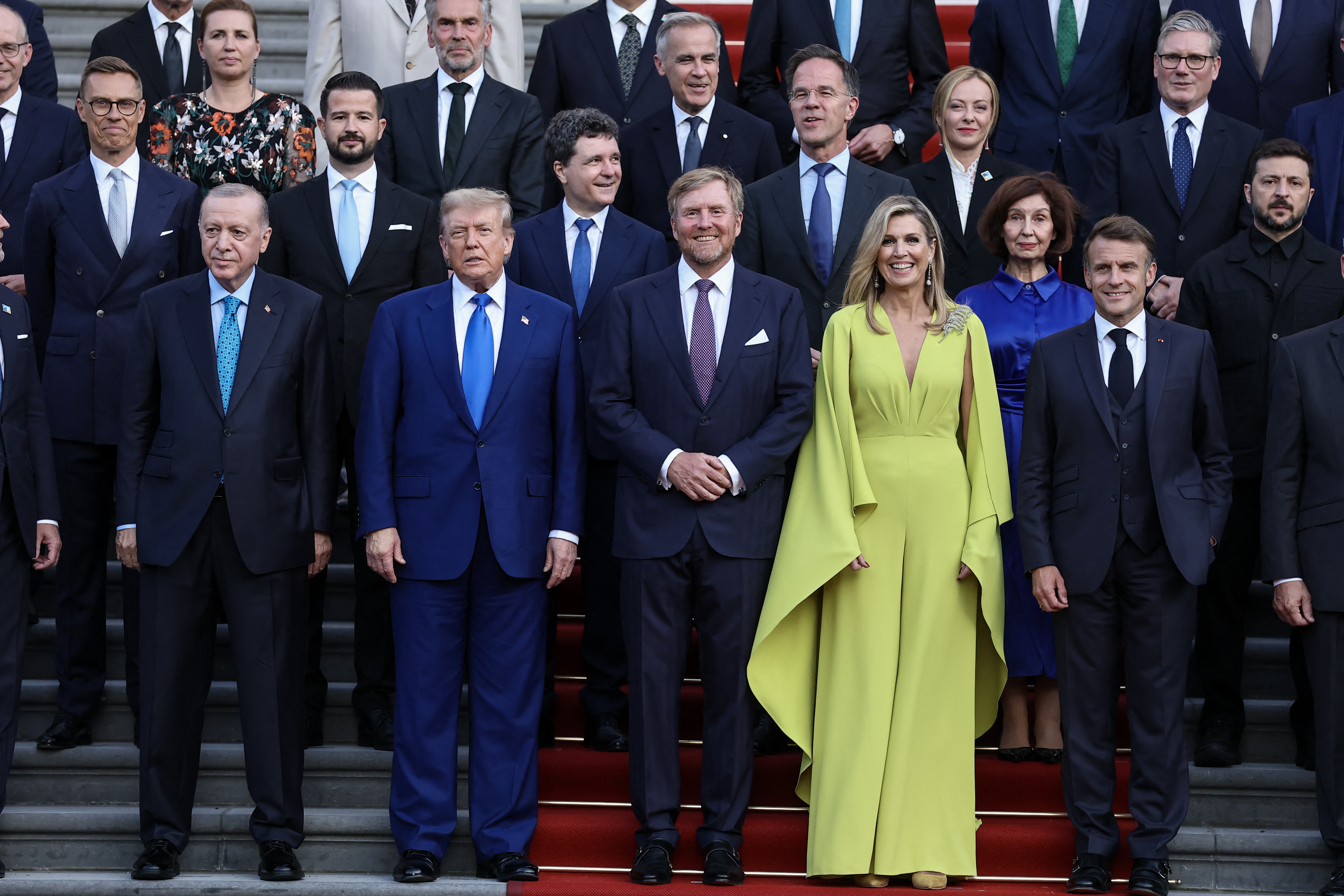 In a different shot from the same setting, the atmosphere appears more formal, with leaders wearing serious expressions for an official portrait. Turkey's President Recep Tayyip Erdogan, Trump, King Willem-Alexander, Queen Máxima, and Macron pose alongside other NATO country leaders for the family photo.