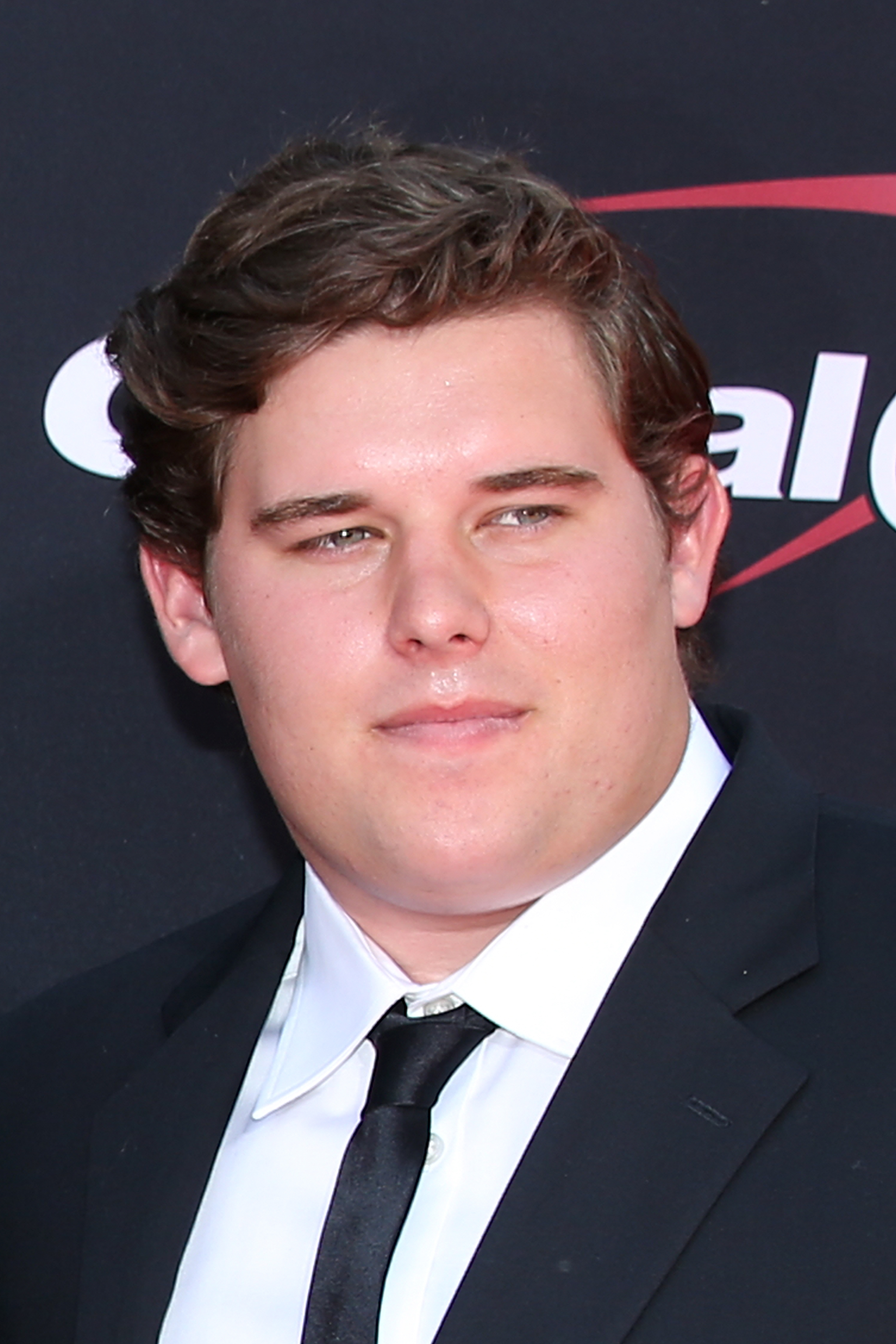 Christopher Schwarzenegger attends the 2017 ESPYS at the Microsoft Theater in Los Angeles. Wearing a classic black suit with a crisp white shirt and black tie, he appears clean-shaven with neatly styled hair and a fuller face, presenting a polished look on the red carpet.