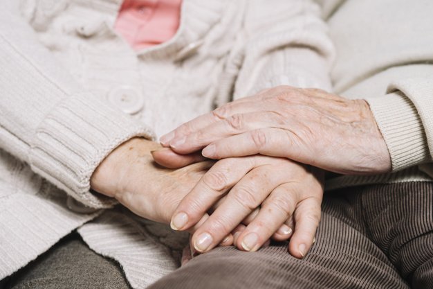 Elderly couple holding hands while sitting together at home. | Source: Freepik