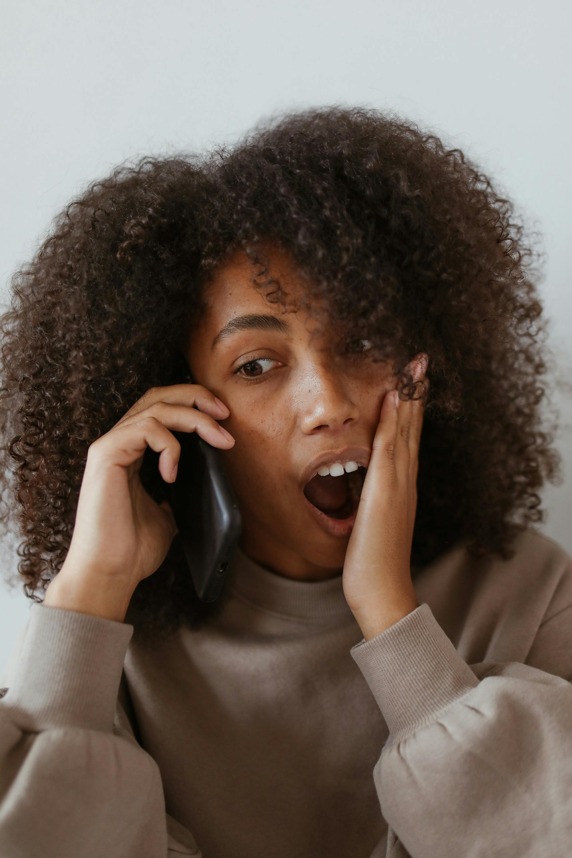 A woman reacting in shock while talking on the phone | Source: Pexels