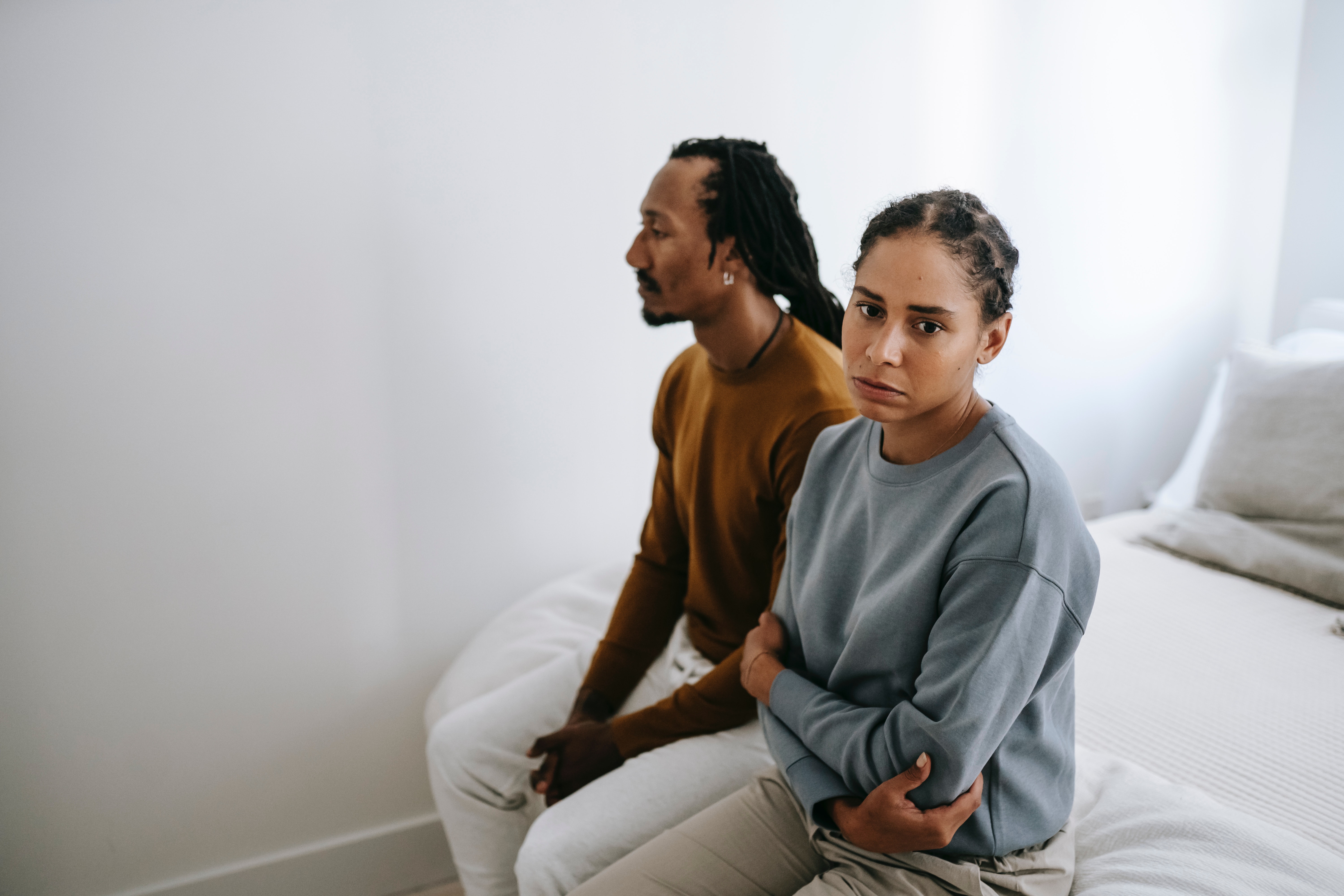 Unhappy black couple sitting on bed together. | Source: Pexels