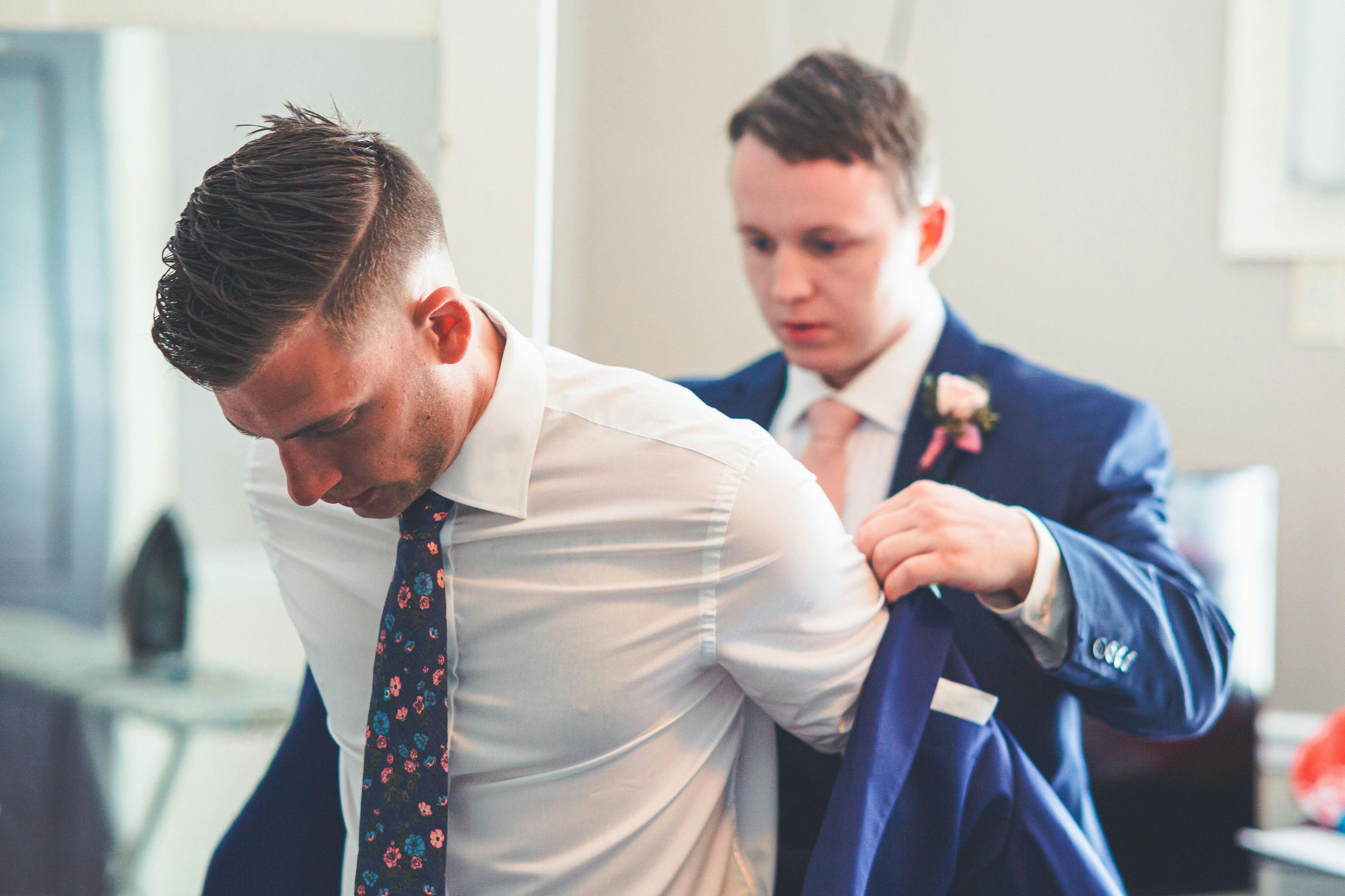 For illustration purposes only. Groomsman helps his brother put on his suit jacket | Source: Pexels