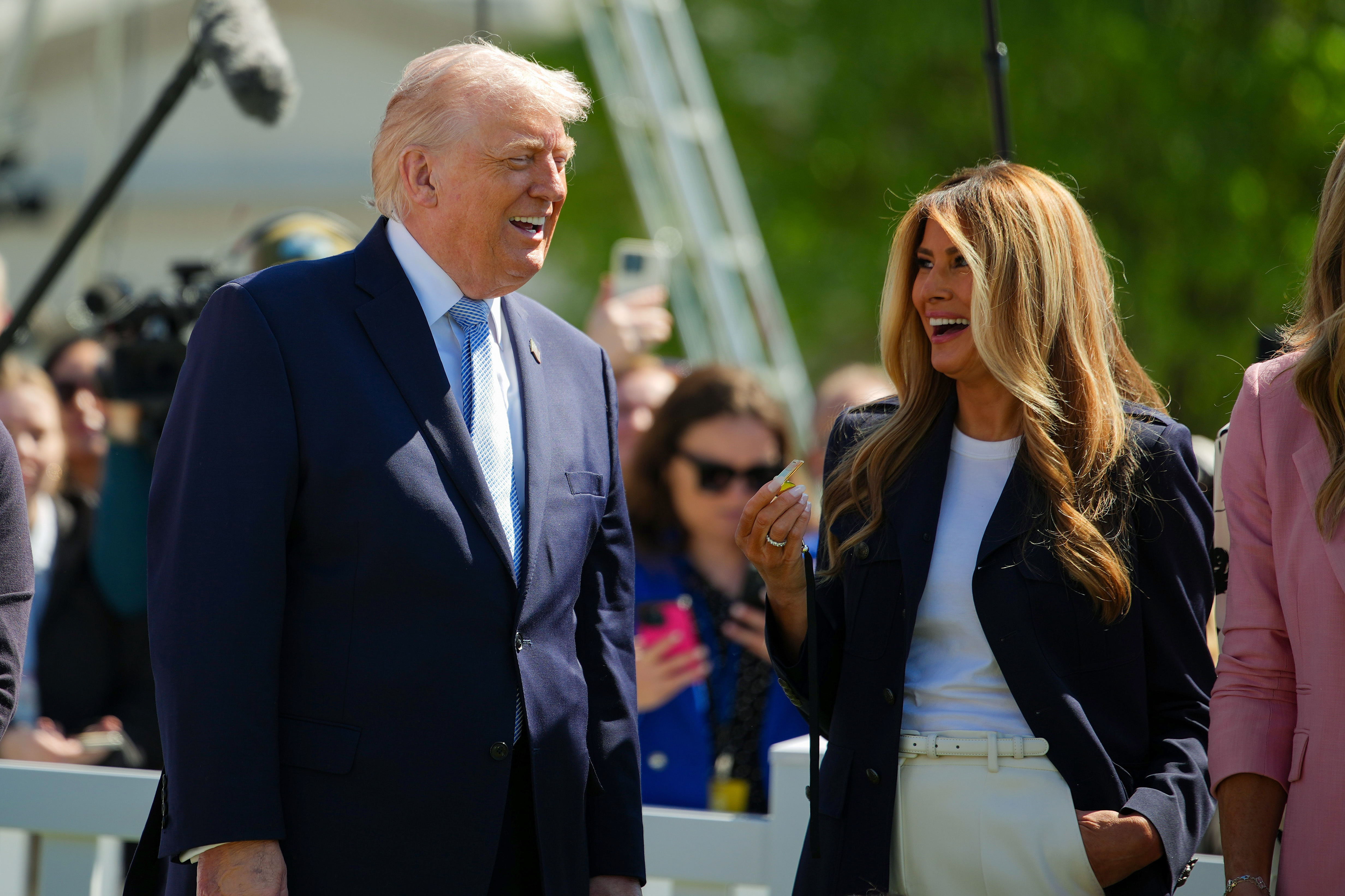 Donald and Melania Trump share a light-hearted moment on the South Lawn, with Melania holding a whistle amid the cheerful crowd.