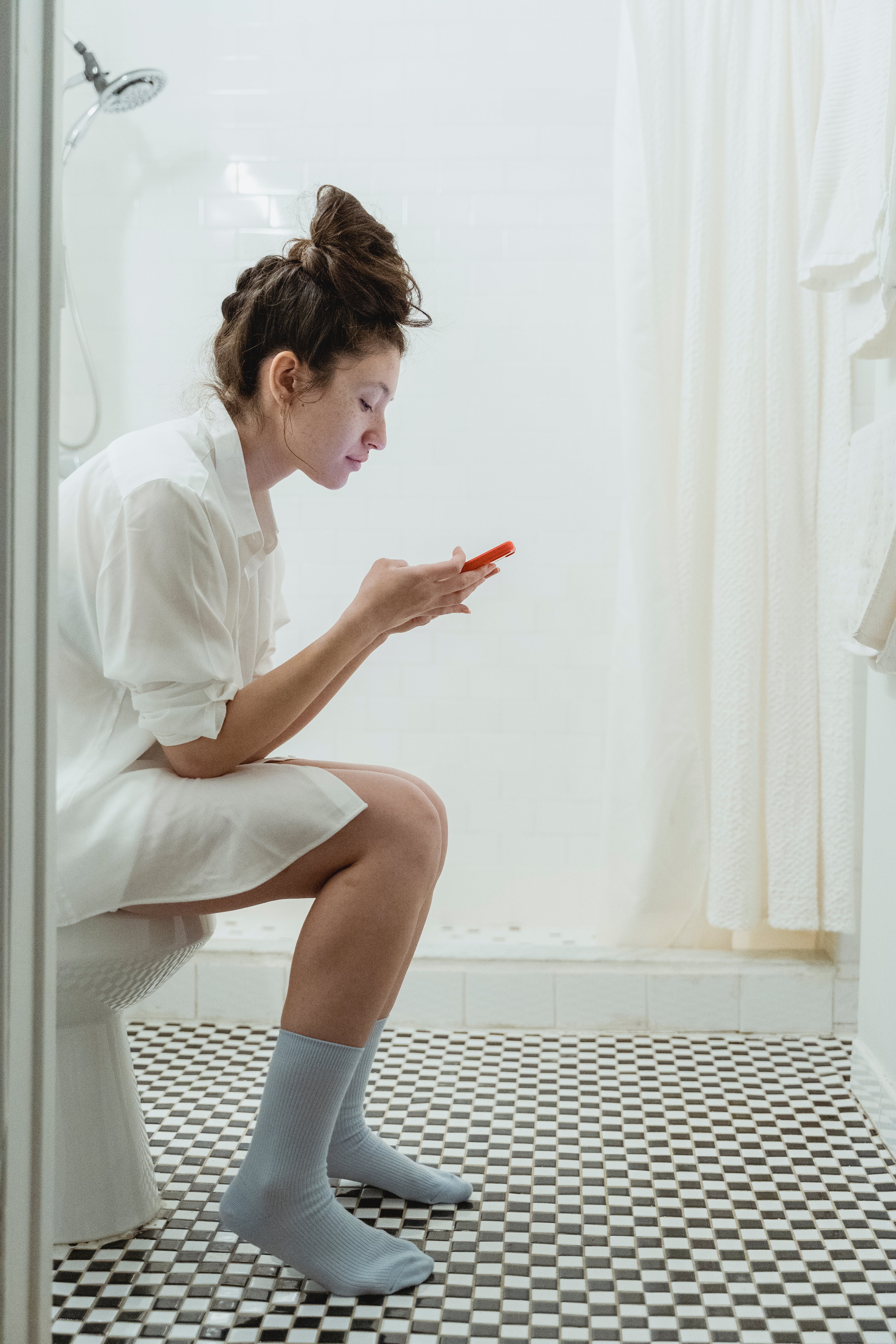 A woman sitting on a toilet using her phone. | Source: Pexels