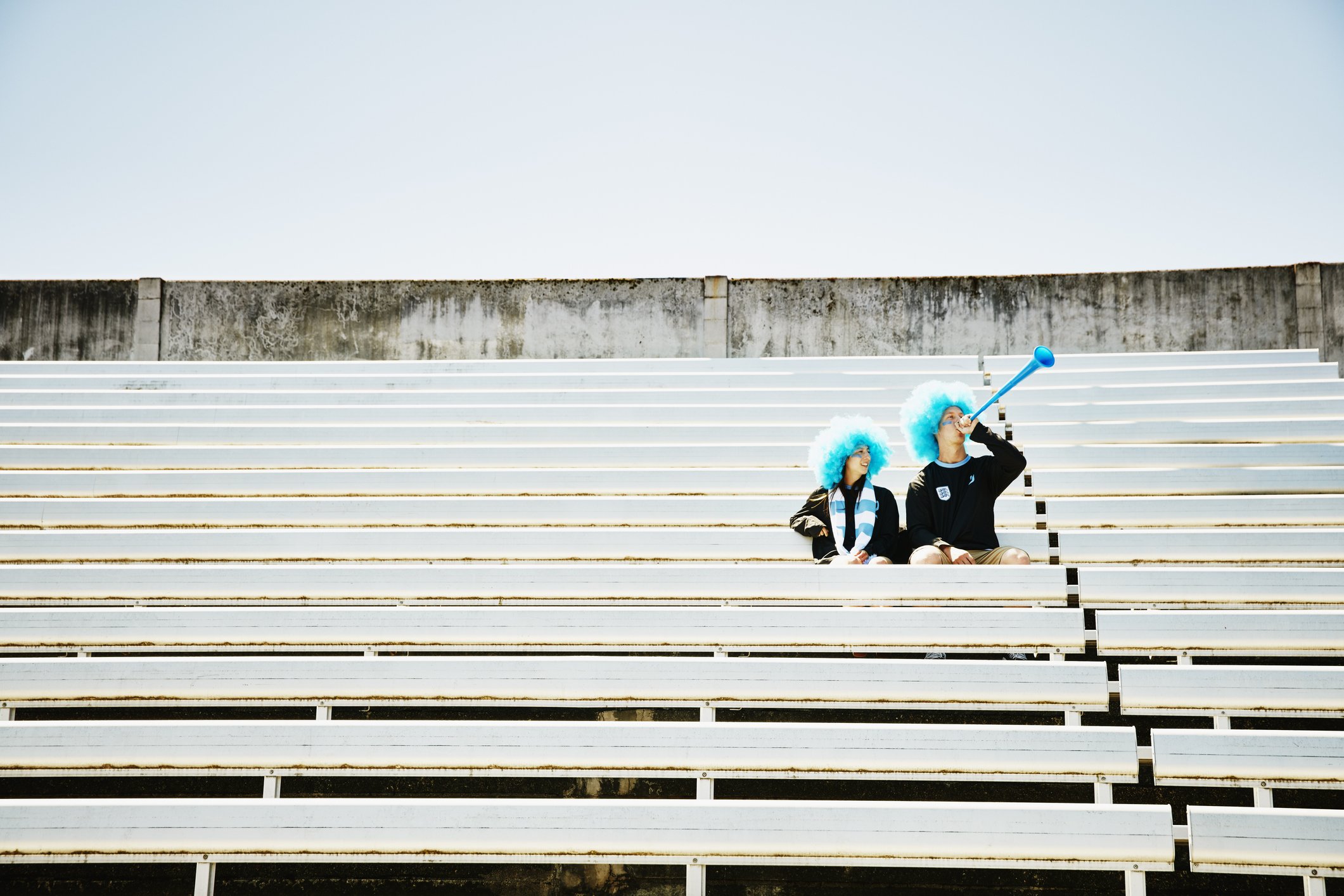 Ein Paar mit Perücken und Mannschaftsuniformen bläst vor dem Fußballspiel im leeren Stadion Vuvuzela | Quelle: Getty Images